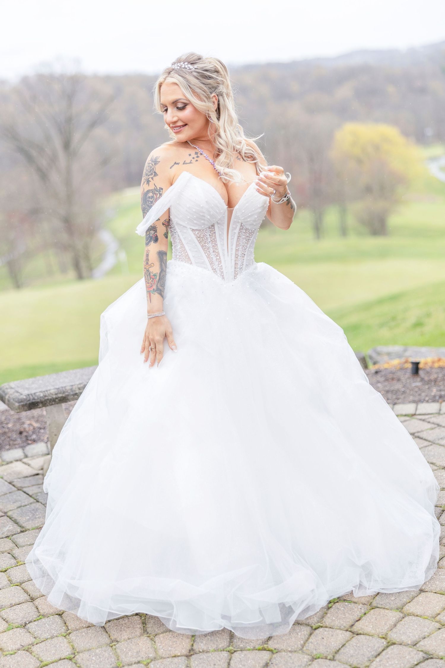 A stunning off-shoulder wedding gown with a corset bodice and full tulle skirt showcased outdoors on a stone patio.