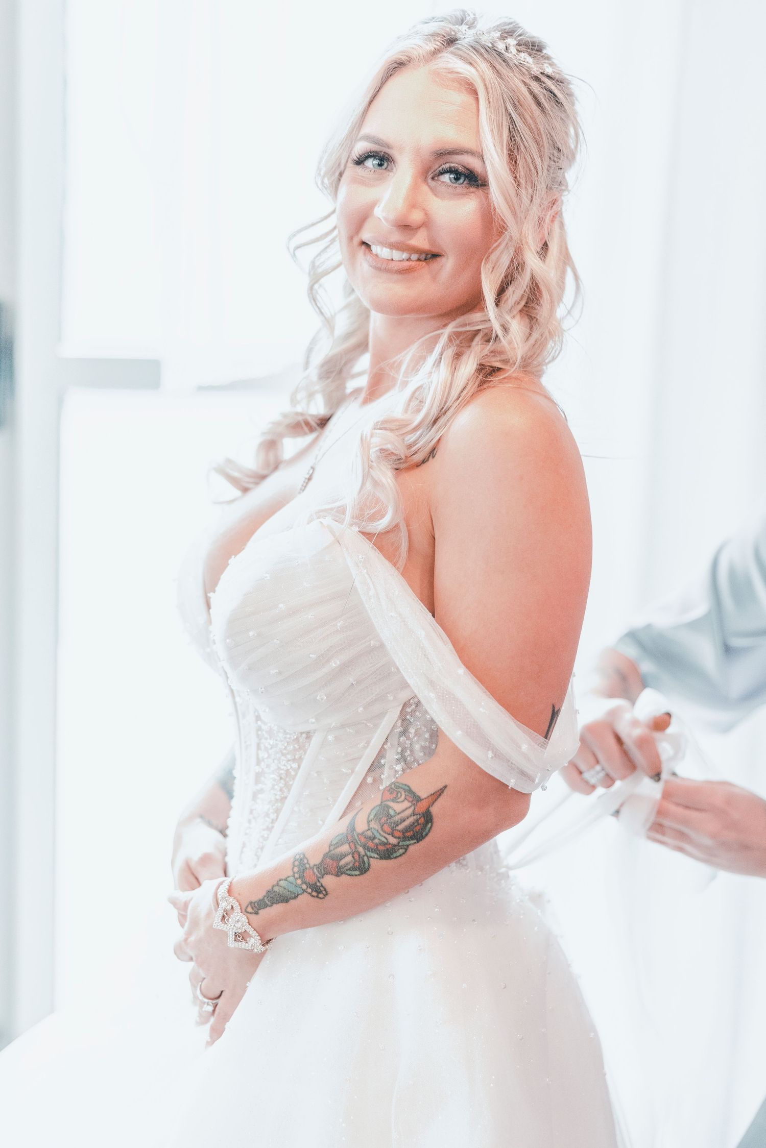 Elegant white wedding dress with off-shoulder design and delicate lace details showcases intricate floral tattoo.