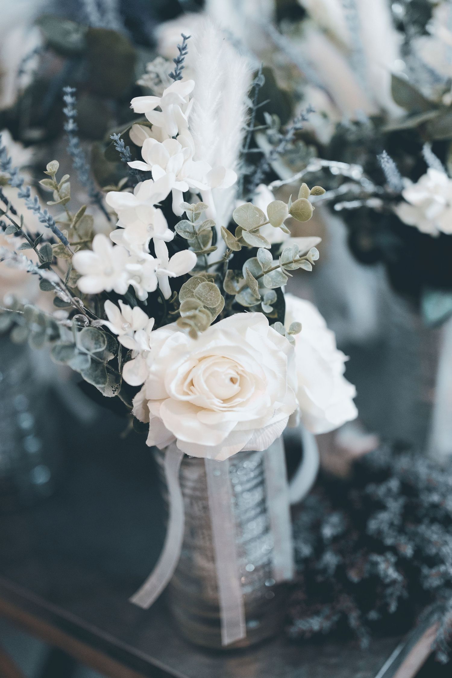 Elegant white rose and eucalyptus floral arrangement in a vase with delicate ribbon accents in moody lighting.