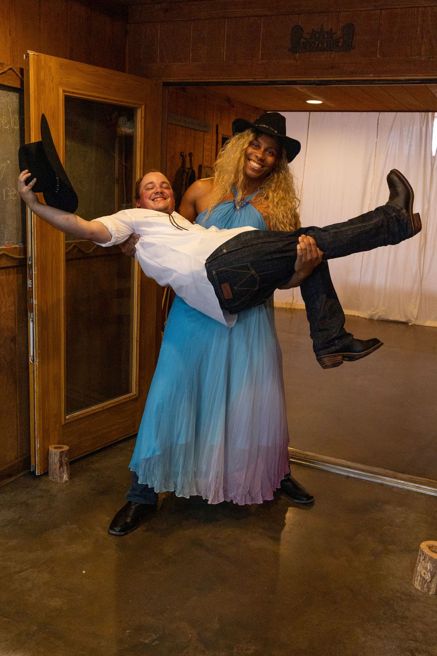 A playful moment captured as someone in blue dress lifts another person wearing western attire.