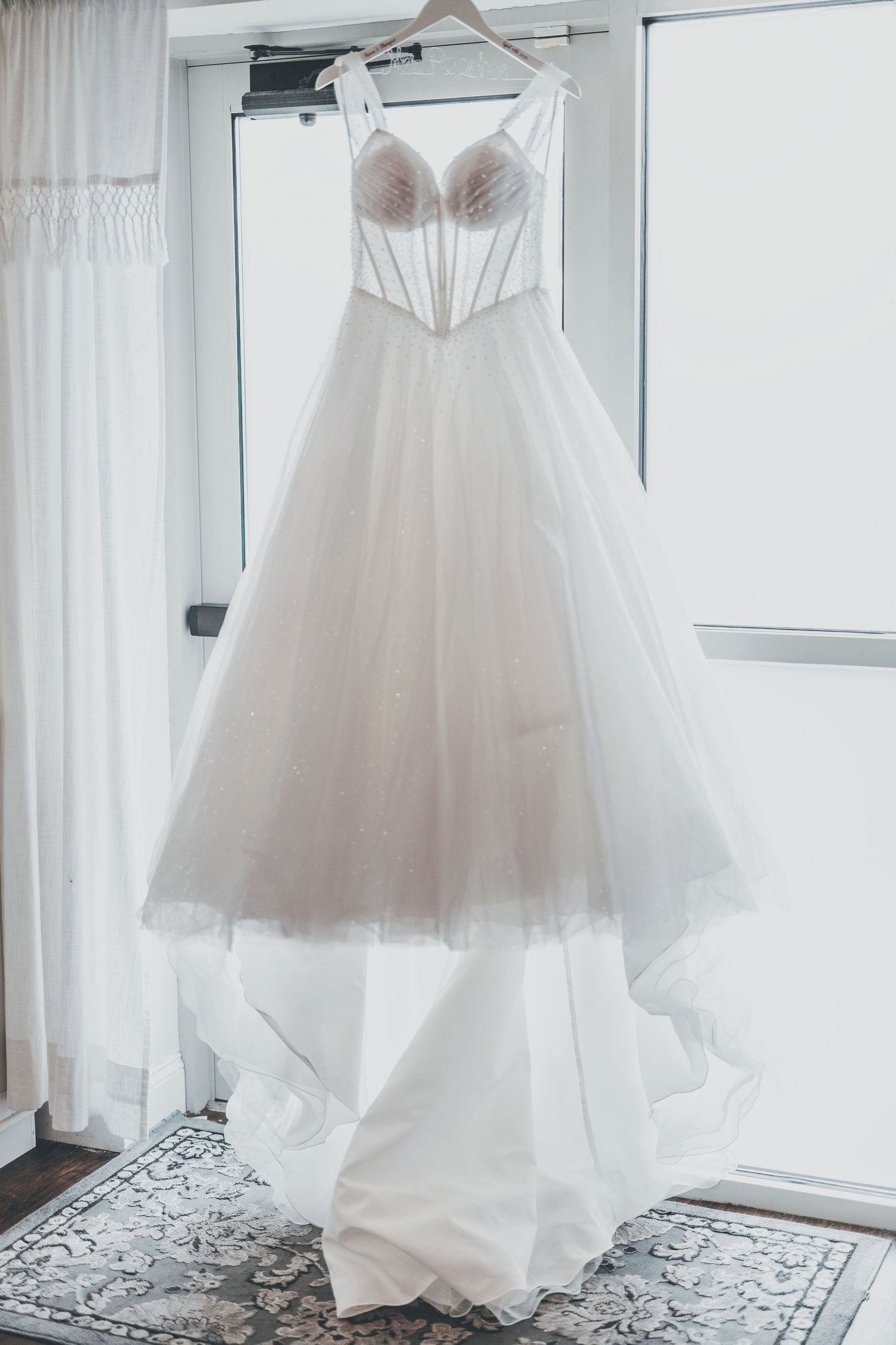 A white wedding dress with a fitted lace bodice and flowing tulle skirt hangs elegantly against a light backdrop.
