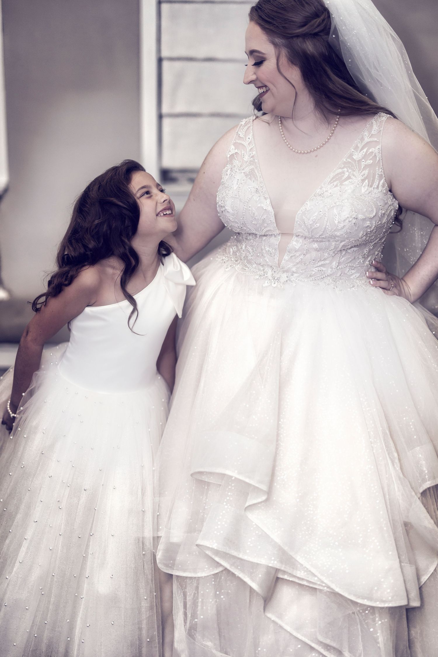 Two people in beautiful white wedding dresses share a joyful moment together outdoors.