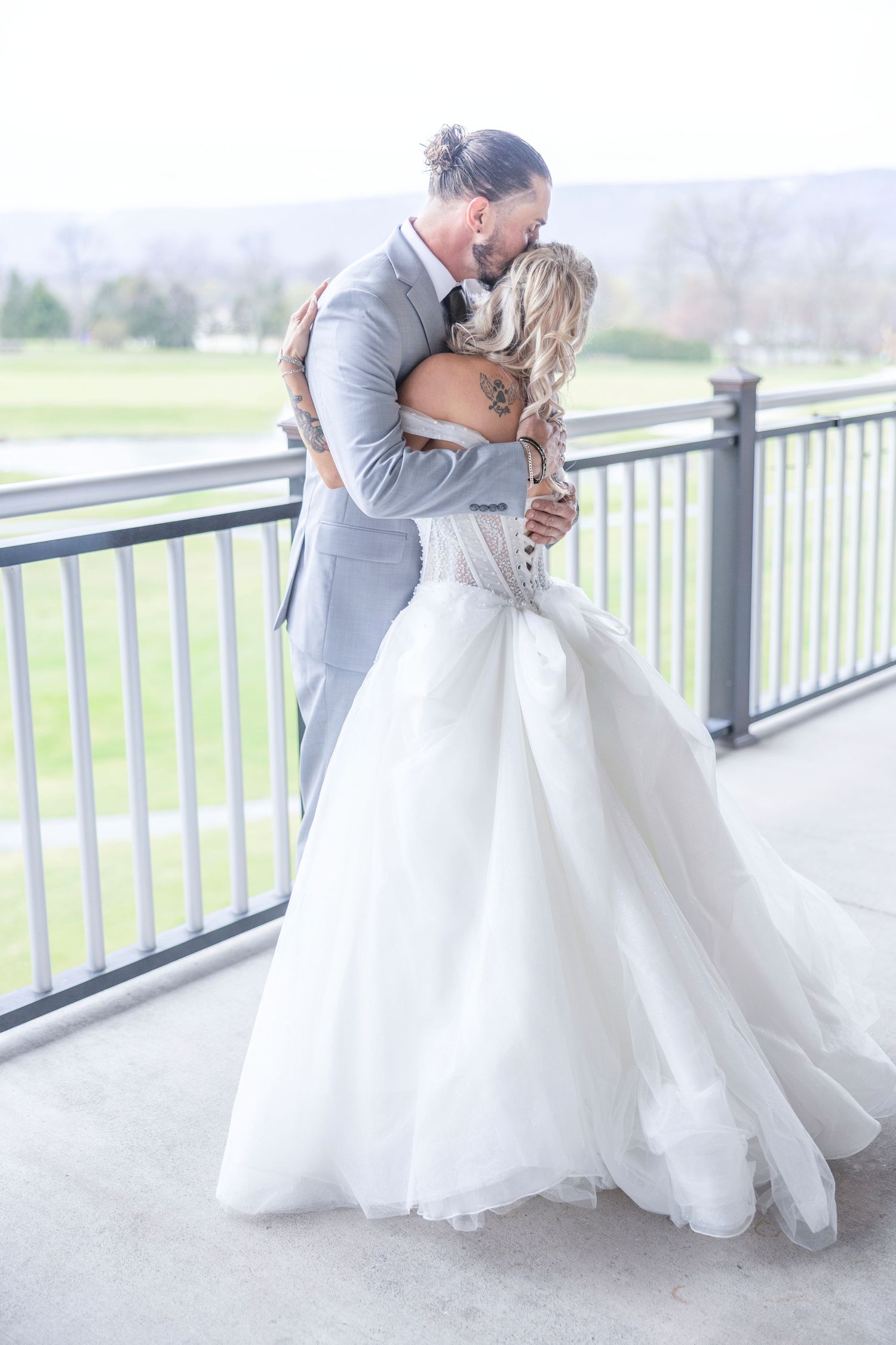 A romantic wedding moment between a couple embracing on a balcony, bride in a flowing white gown and groom in gray suit.