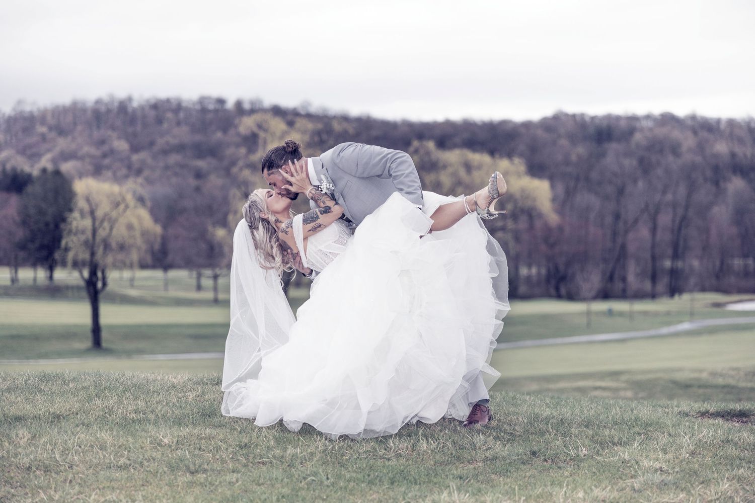 A romantic posed photograph in a grassy meadow on an overcast spring day.