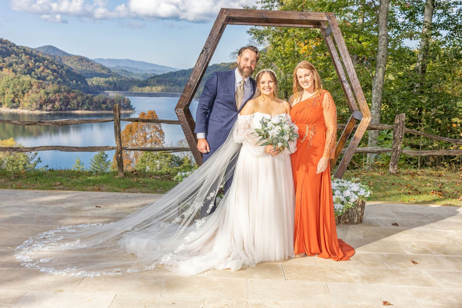 Outdoor wedding ceremony with large hexagonal arch set against a scenic mountain lake backdrop.