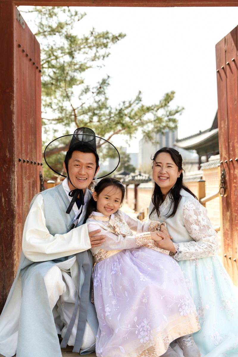 A group poses playfully in traditional Korean hanbok attire at a historic building.