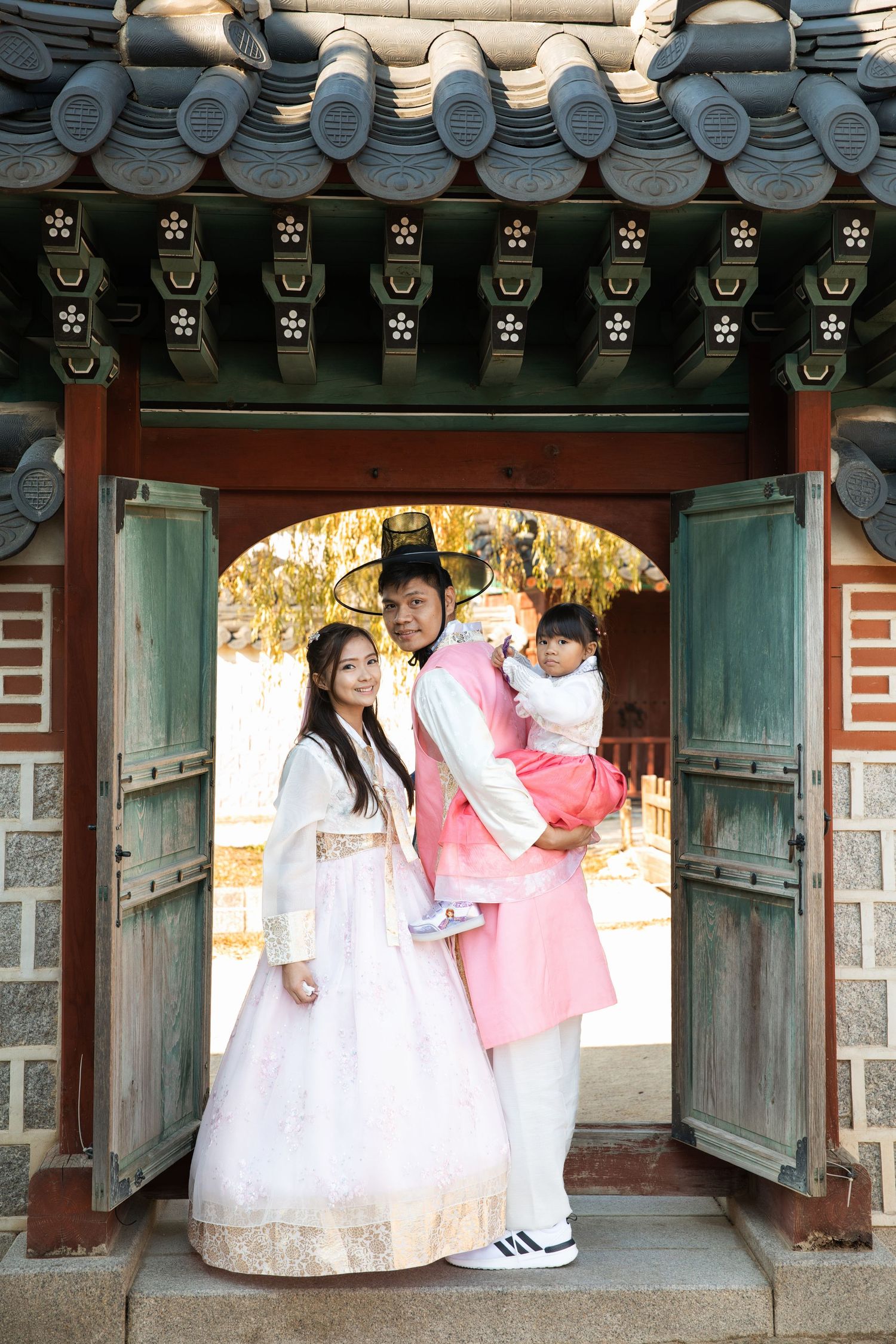 Traditional Korean hanbok outfits worn under ornate temple doorway with decorative roof tiles and green wooden doors.