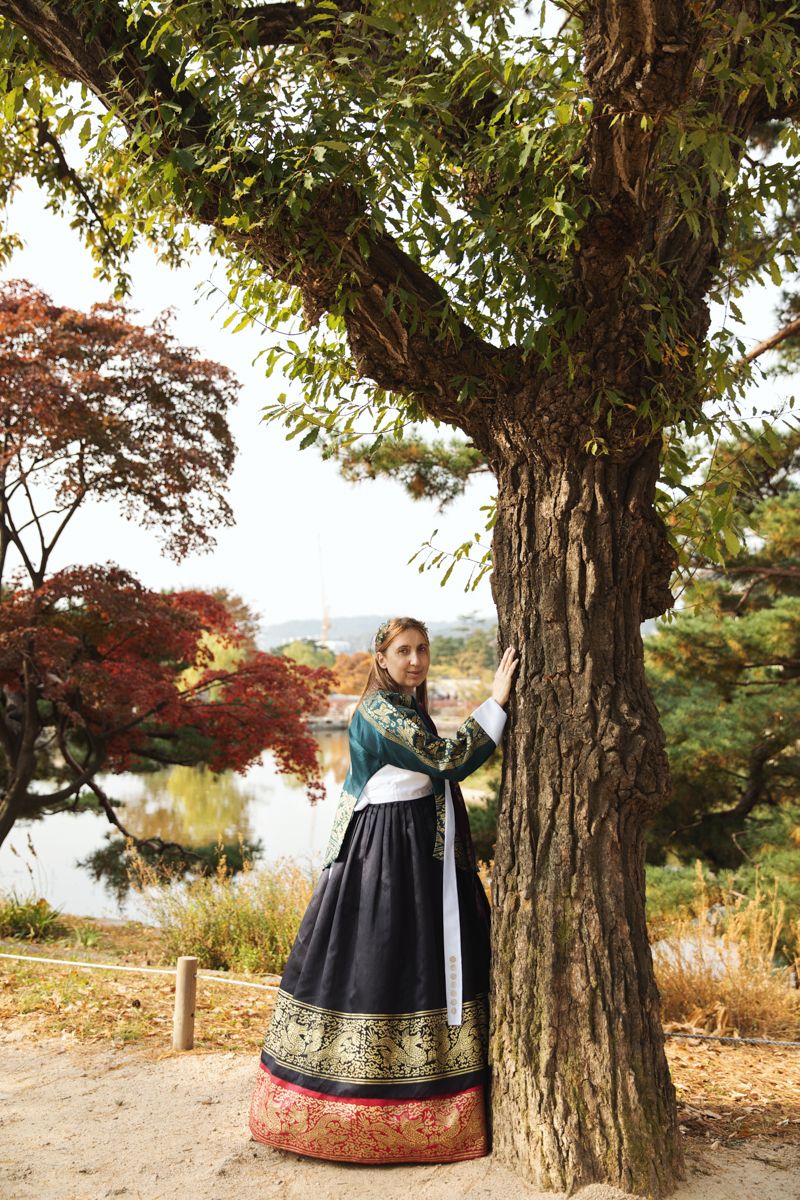 A women wearing Hanbok at Gyeongbokgung Palace in Seoul in front of the lake during the autumn foliage looking at the camera