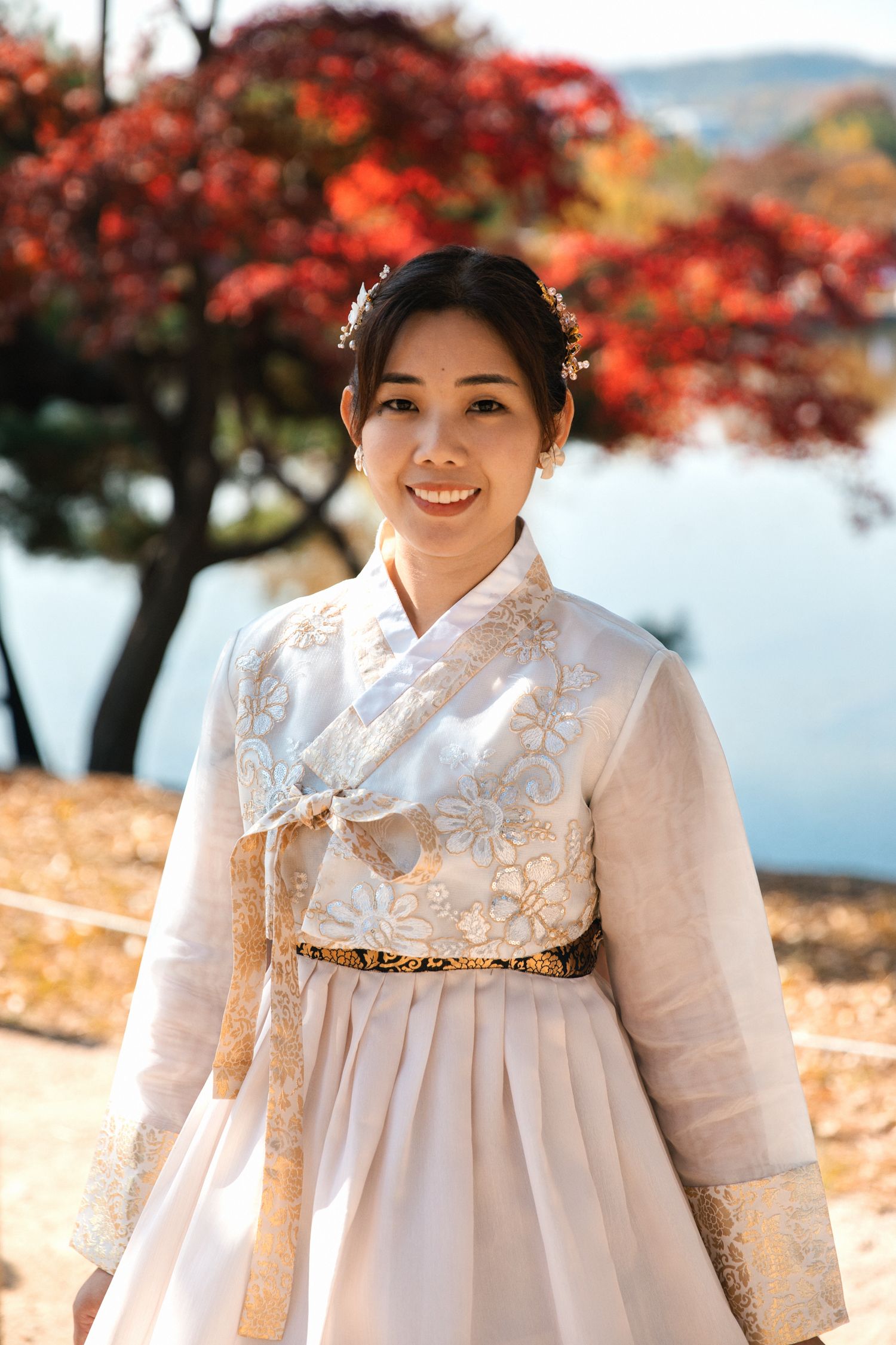 Traditional white Korean hanbok dress with ornate details photographed against autumn foliage.