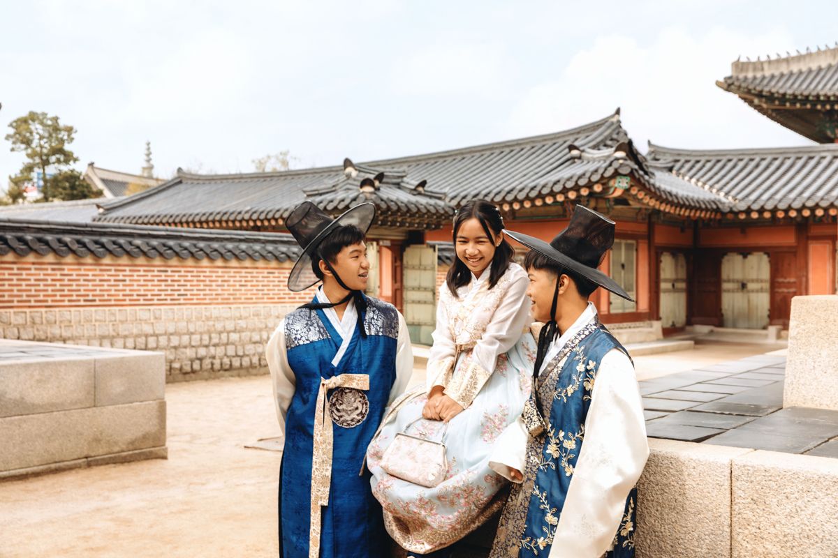Three people in traditional Korean hanbok attire sit together at Gyeongbokgung Palace on a sunny day.