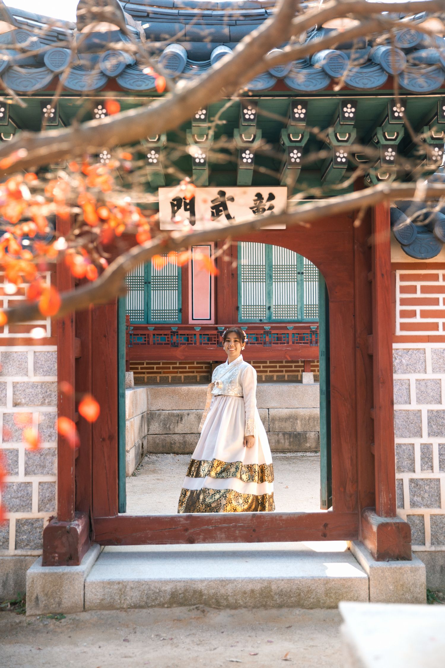 Traditional Korean hanbok dress framed within historic temple gateway during autumn season.