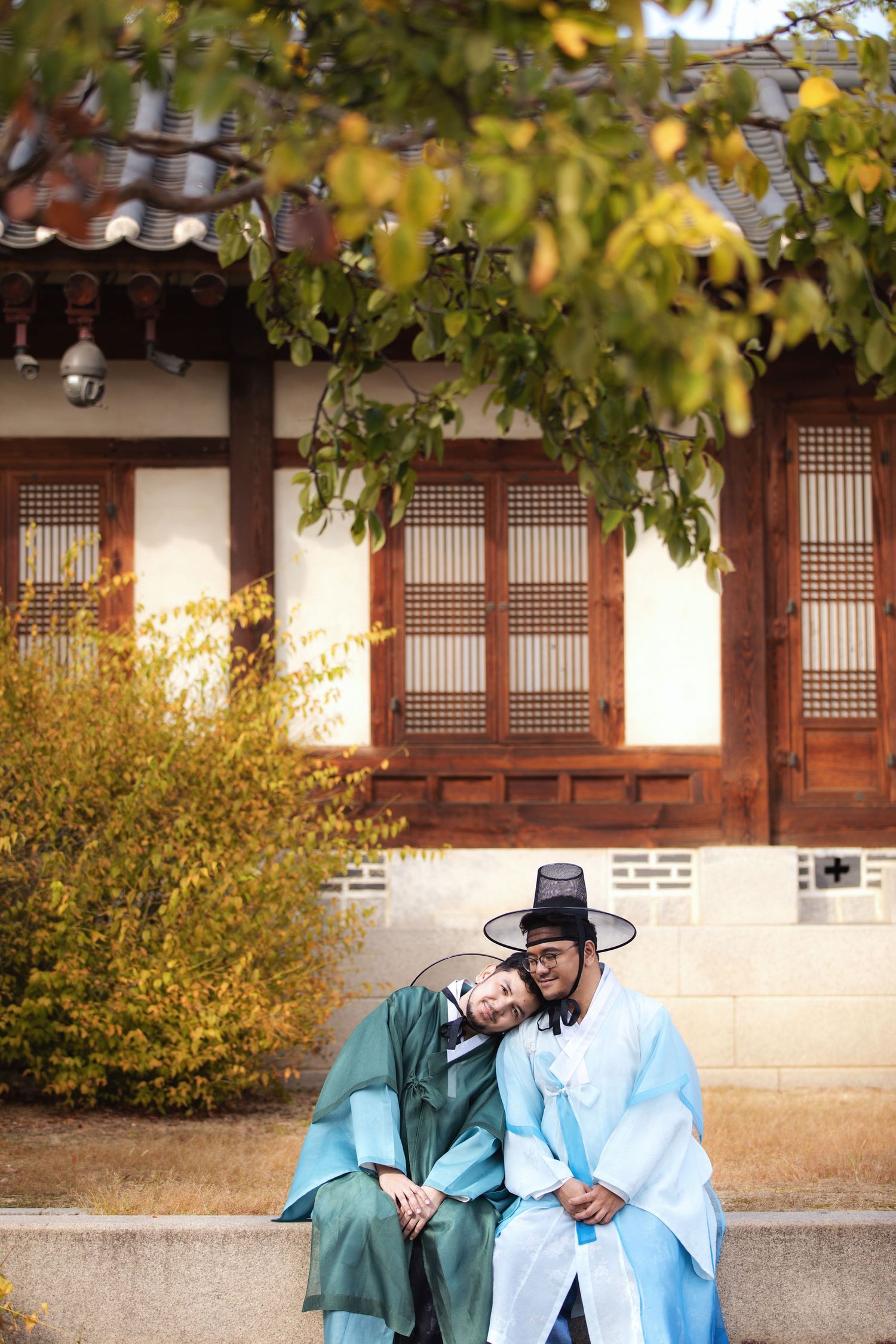 Traditional Korean palace scene with autumn foliage and figures dressed in hanbok sitting on wooden benches.