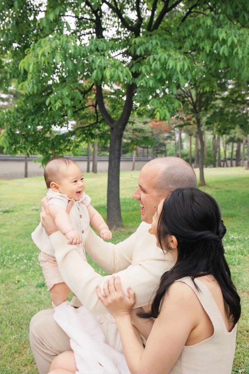 A joyful family moment captured outdoors in a park with green trees on a sunny day.