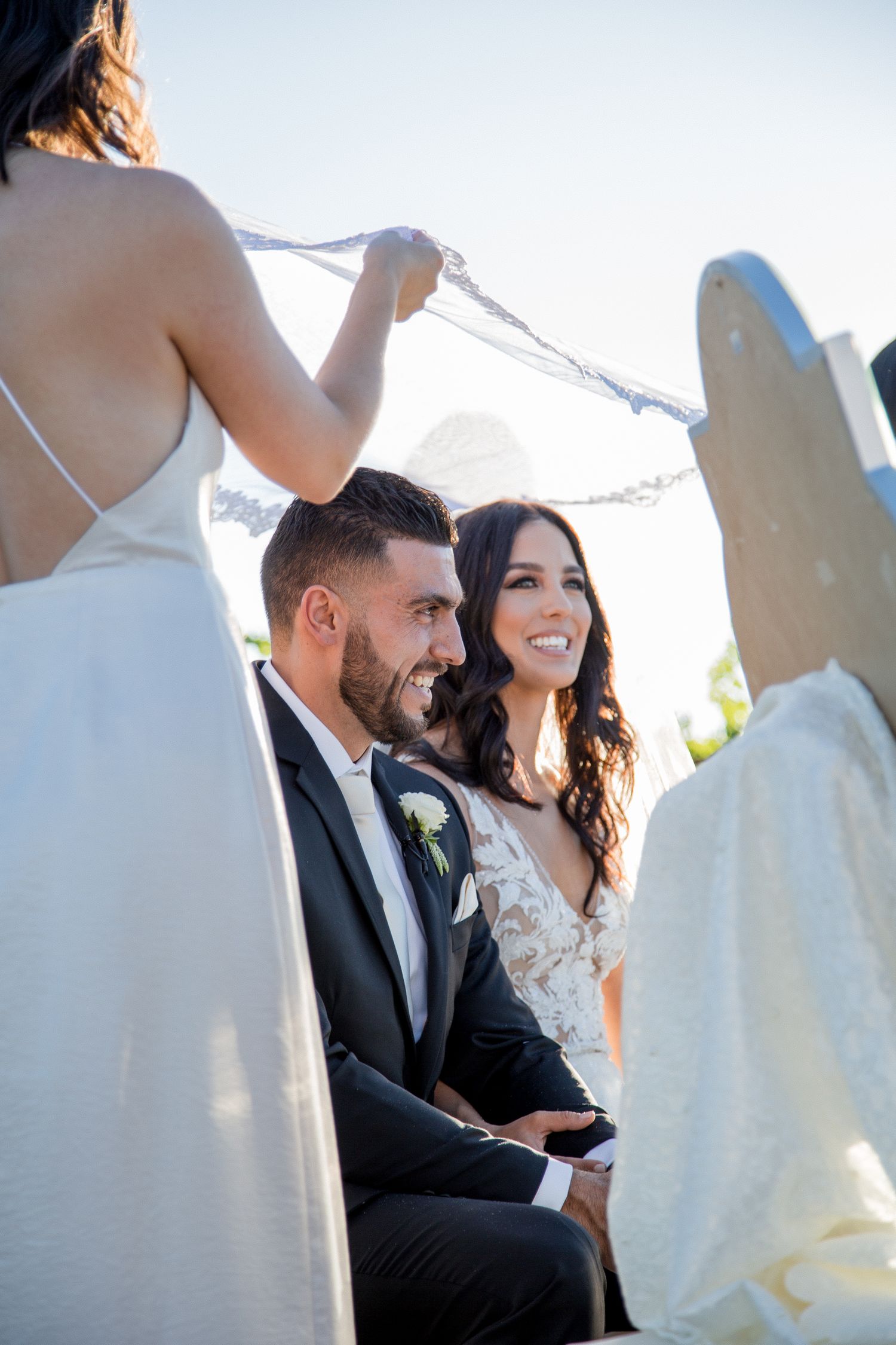 Intimate wedding ceremony moment with couple seated outdoors under bright sky.