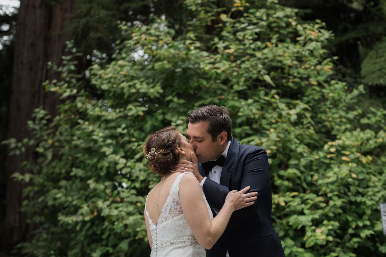 Romantic moment between newlyweds surrounded by lush green foliage.
