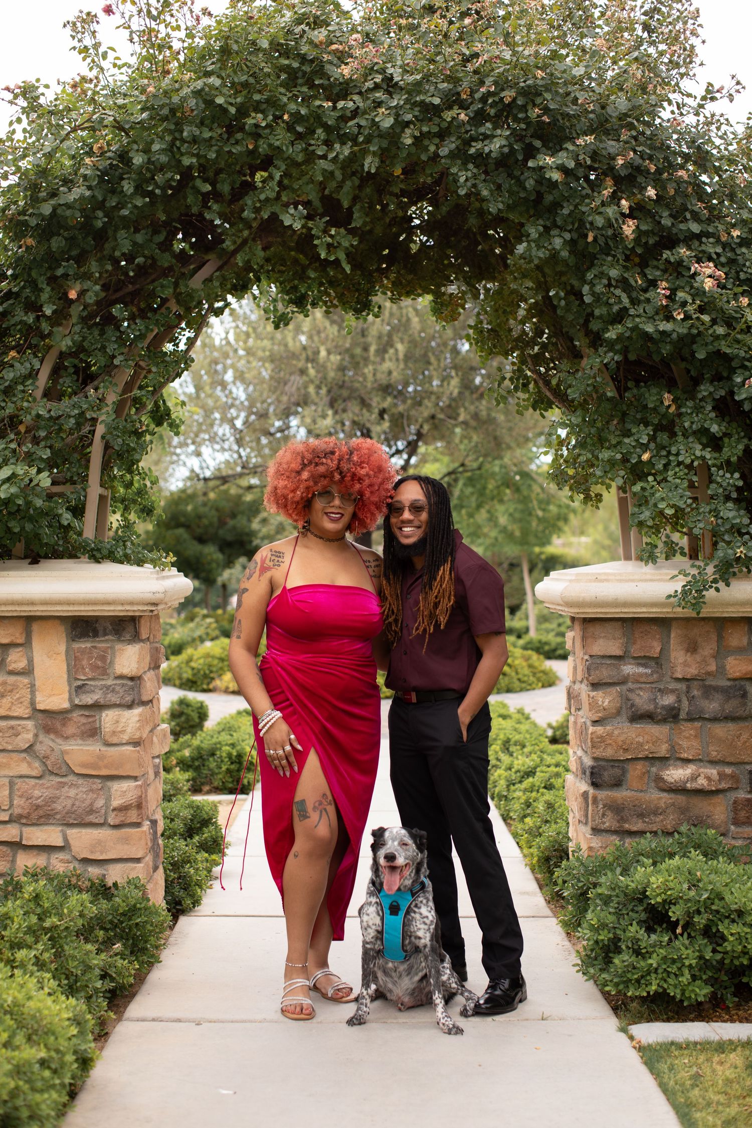 Couple posing with their dog under floral garden arch.