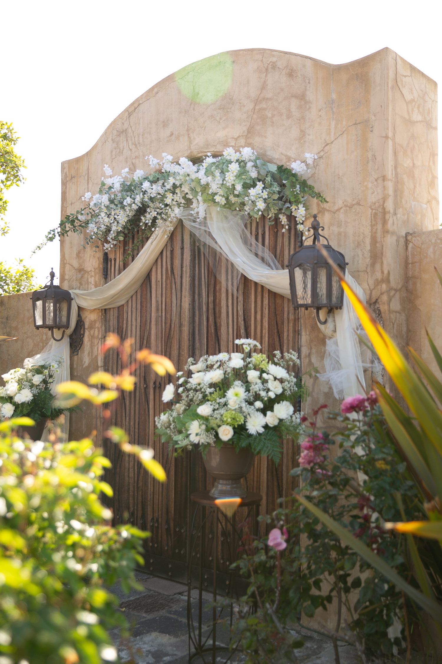 Elegant wedding arch decorated with white flowers and draped fabric in garden setting.