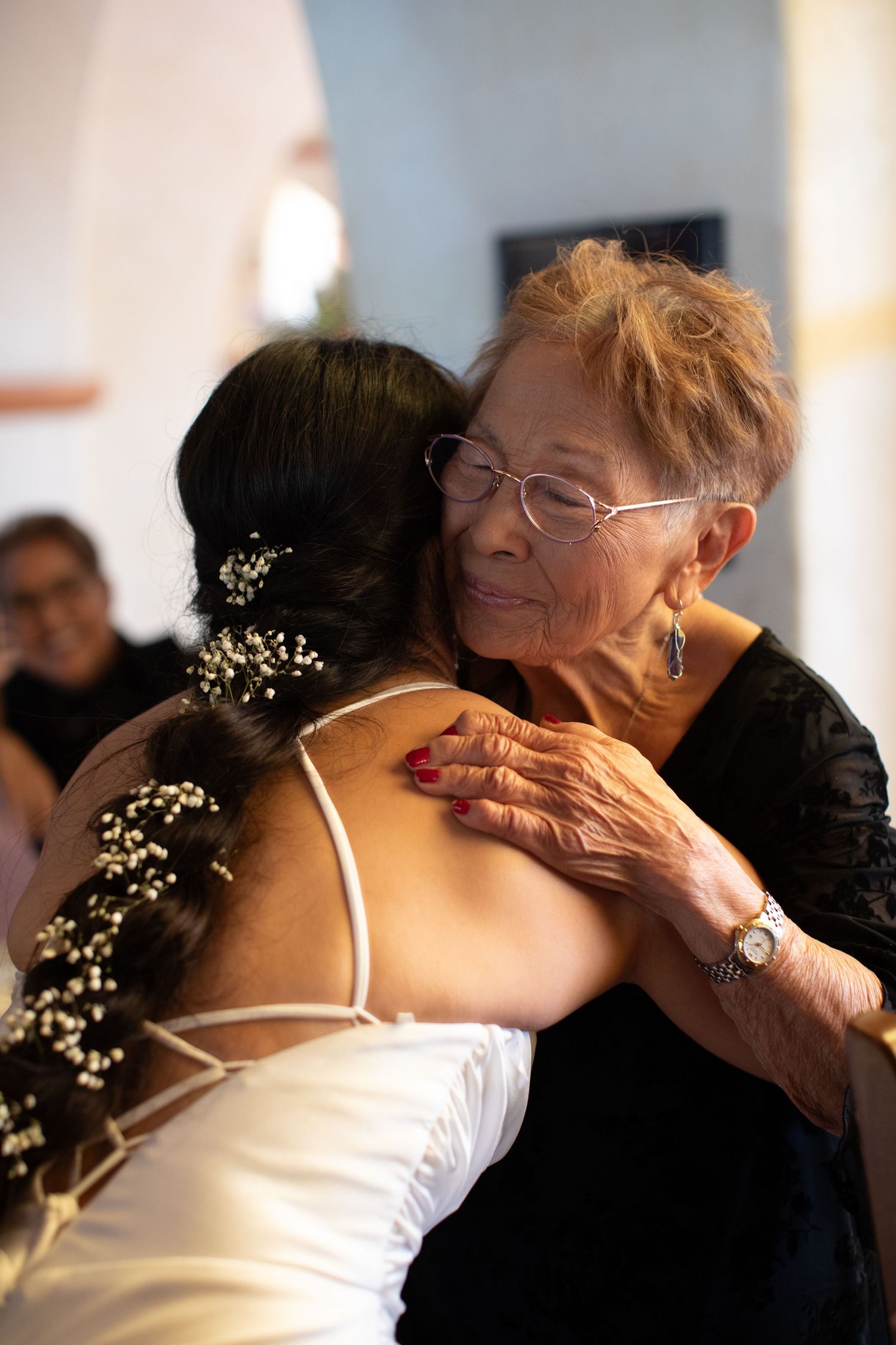 An emotional embrace between a bride in white and an elderly woman wearing black at a wedding.