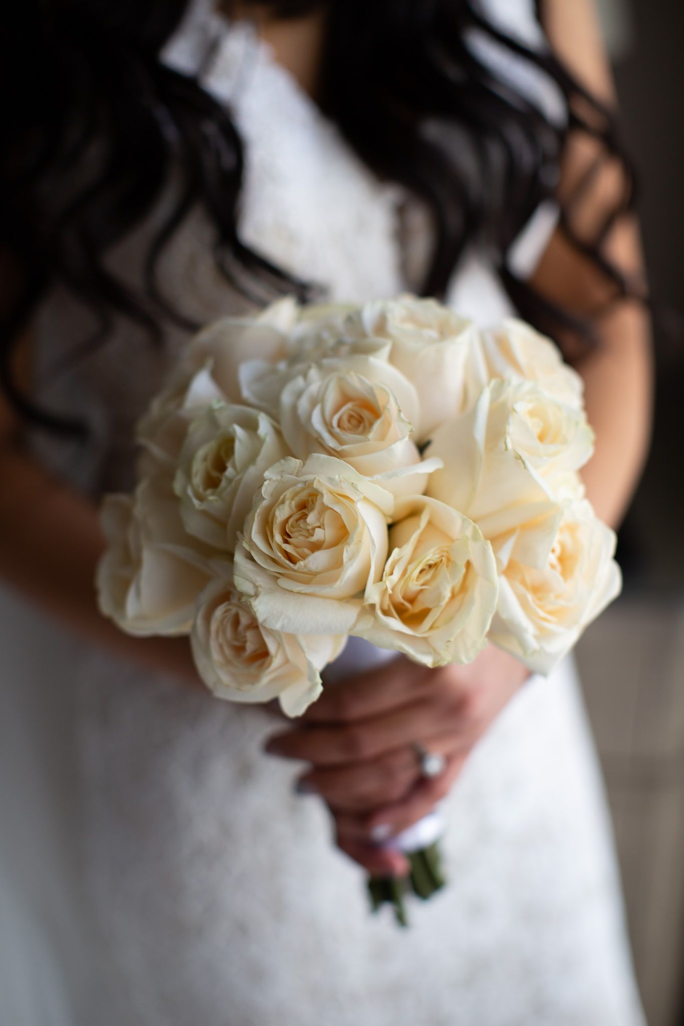 A classic bridal bouquet of cream-colored roses against a white wedding dress.