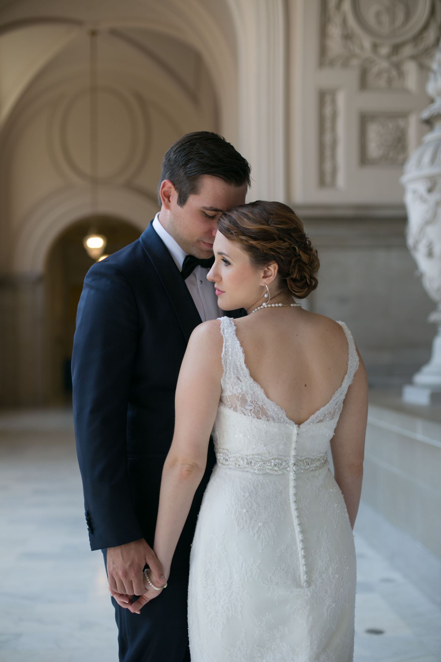 Intimate moment between couple in formal wedding attire against elegant architectural backdrop.