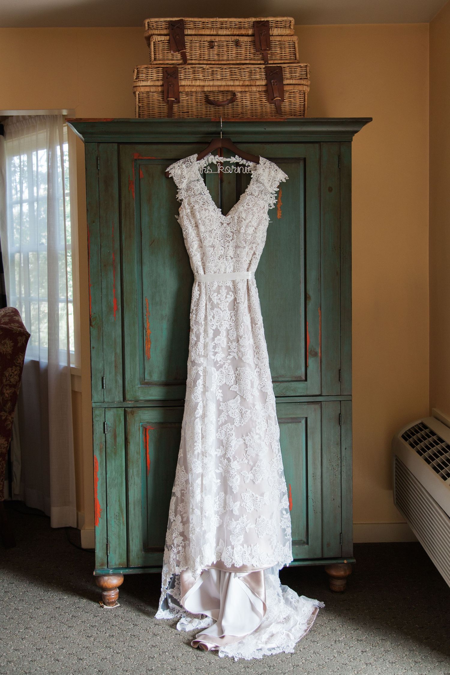 White lace wedding dress hanging on vintage green wooden armoire.