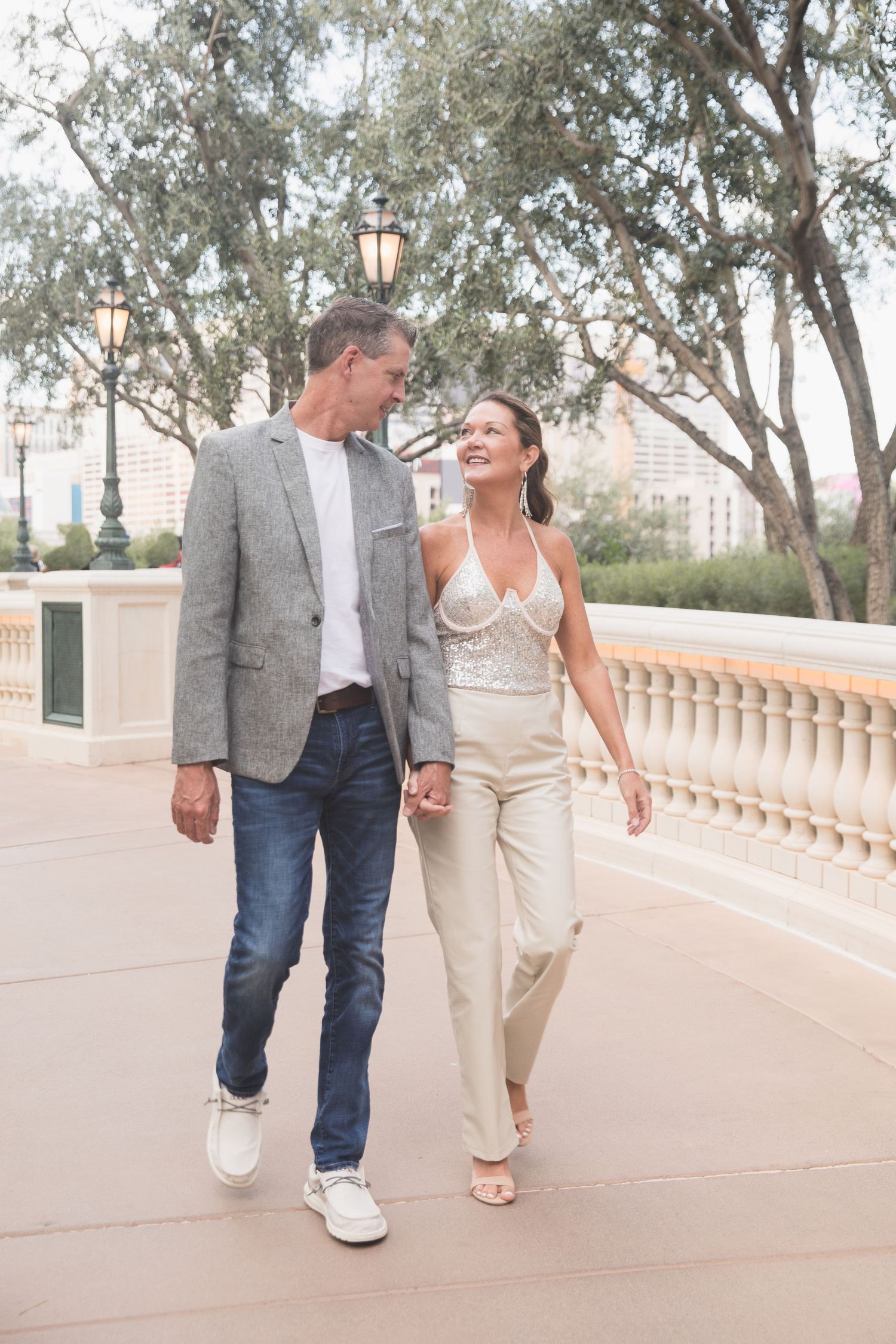 A couple takes a romantic stroll along a tree-lined walkway with classical architecture.