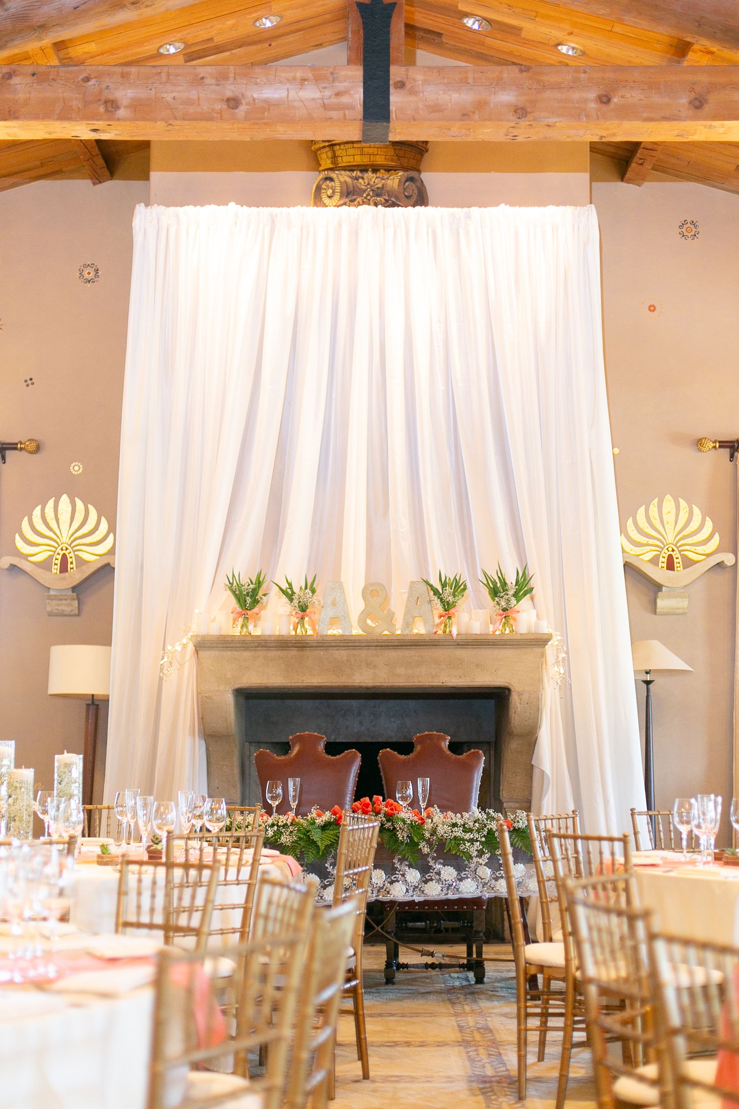 Elegant wedding reception venue with draped white curtains, chandelier, and chiavari chairs.
