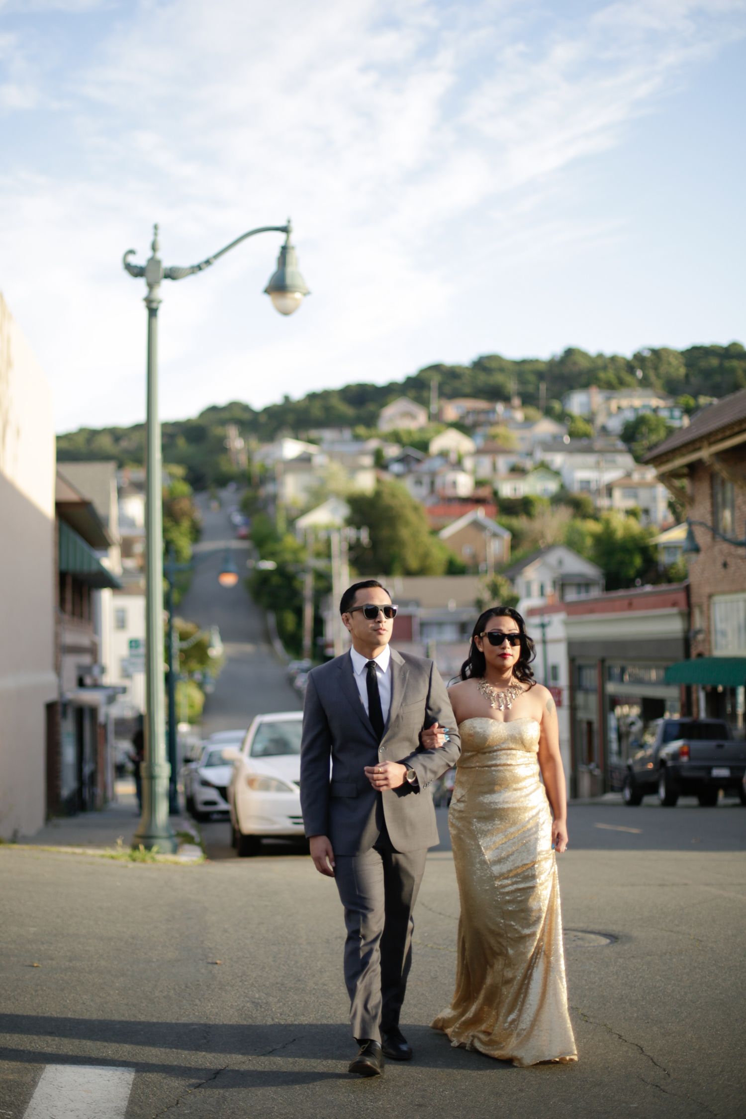 A couple walking down a hill in formal wear with residential houses in the background.