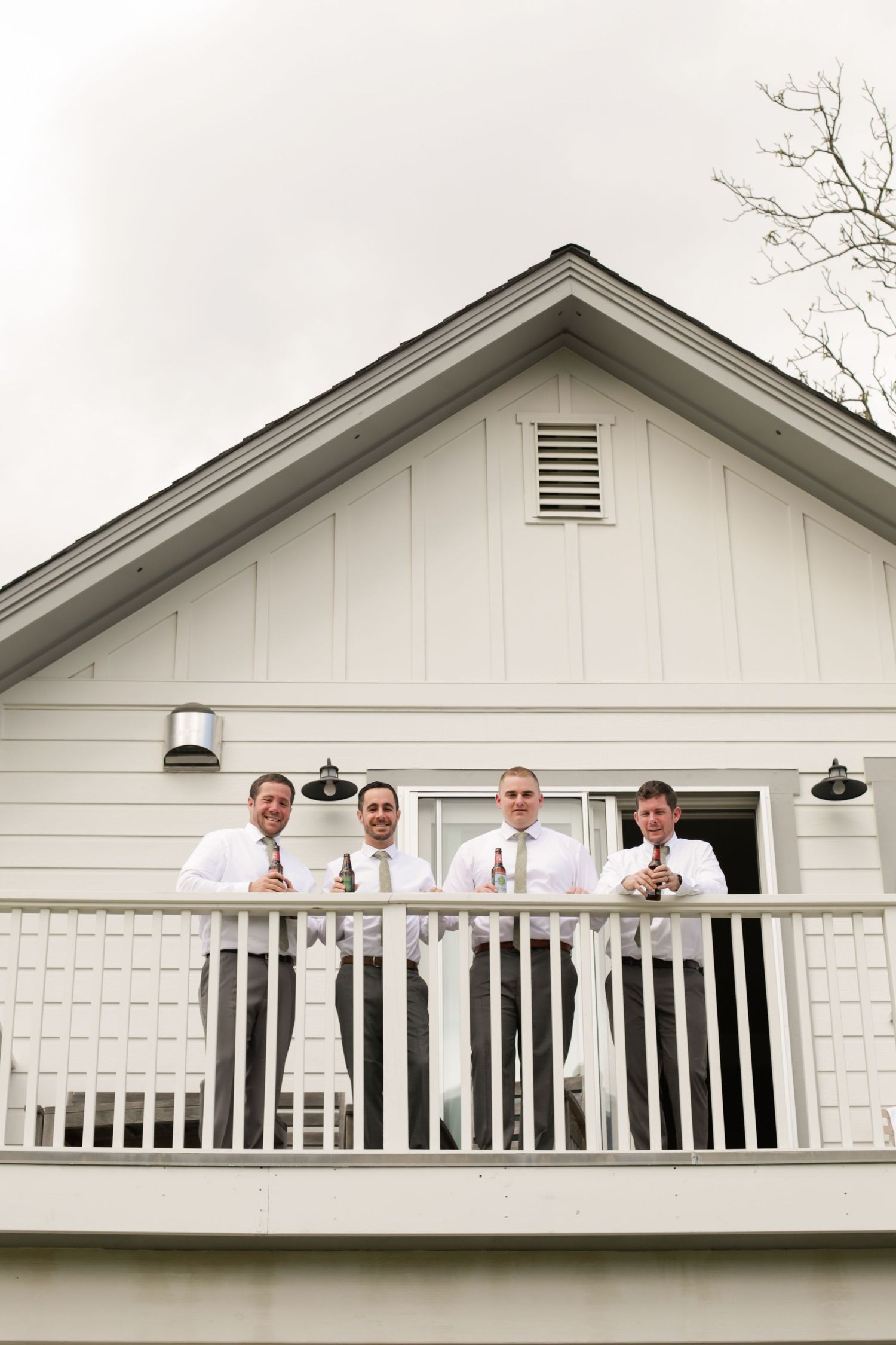 People in formal attire standing on a white balcony of a house.