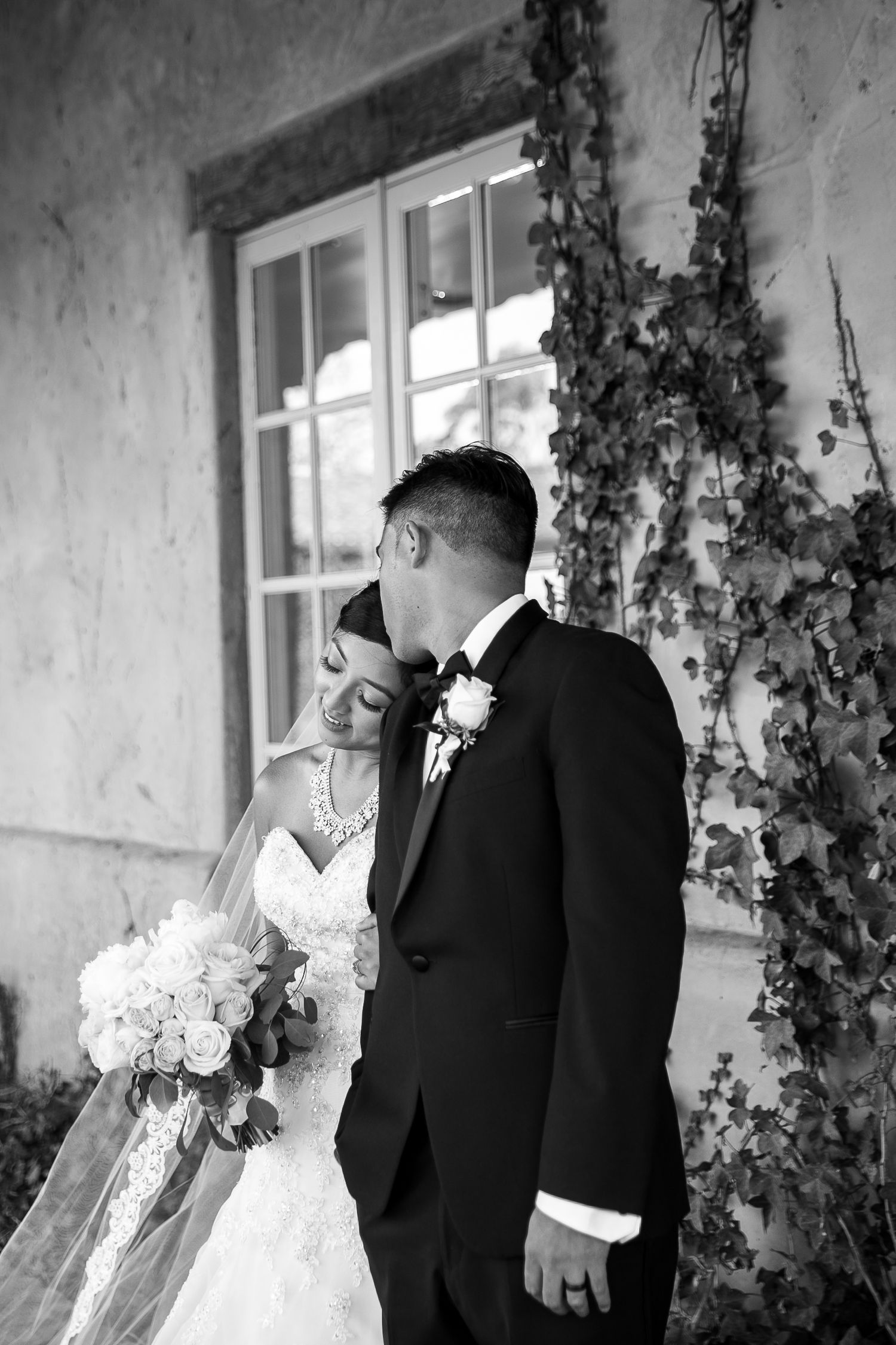 Black and white romantic wedding portrait against ivy-covered wall.