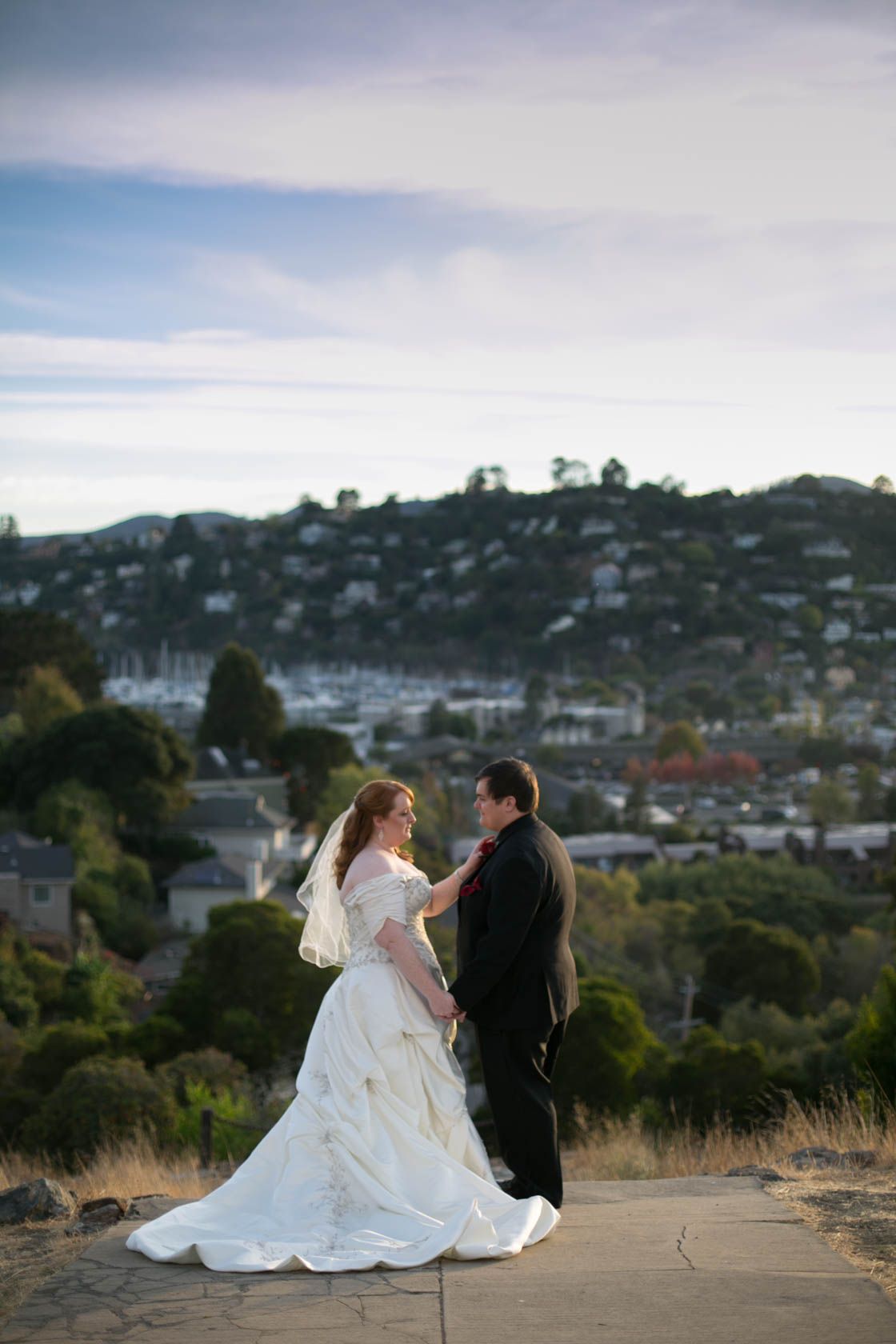A wedding couple standing on hilltop overlooking cityscape at dusk.