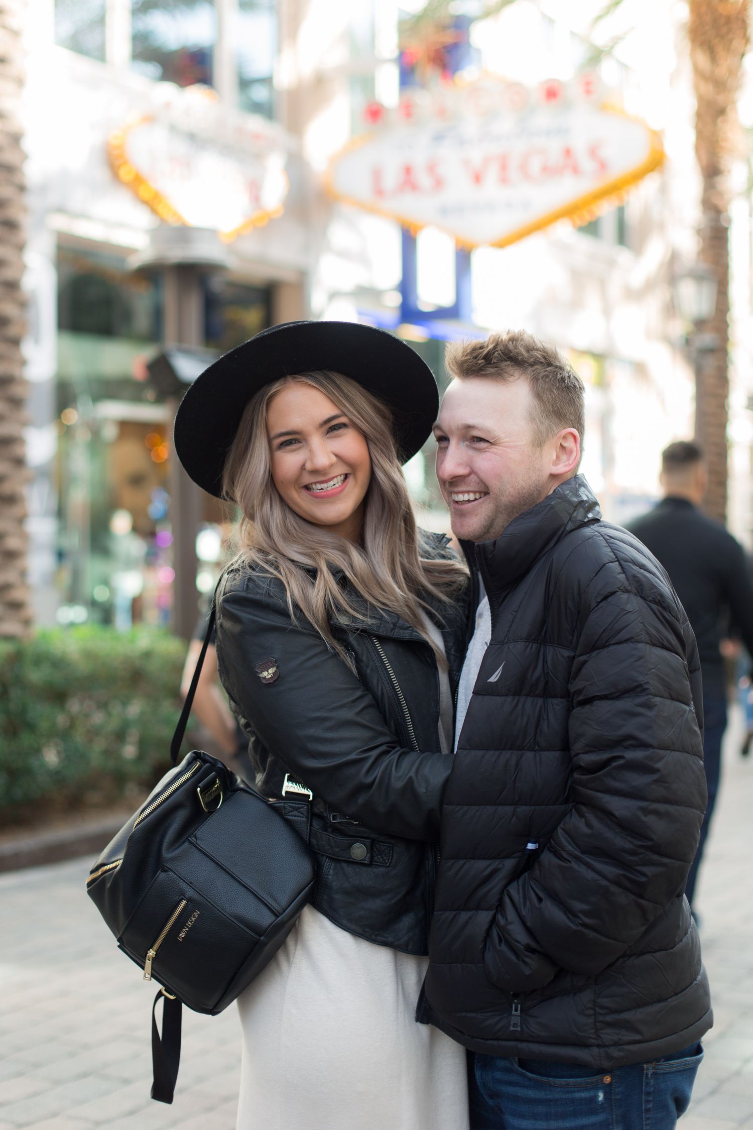 Couple poses happily in front of Las Vegas sign wearing winter outfits.