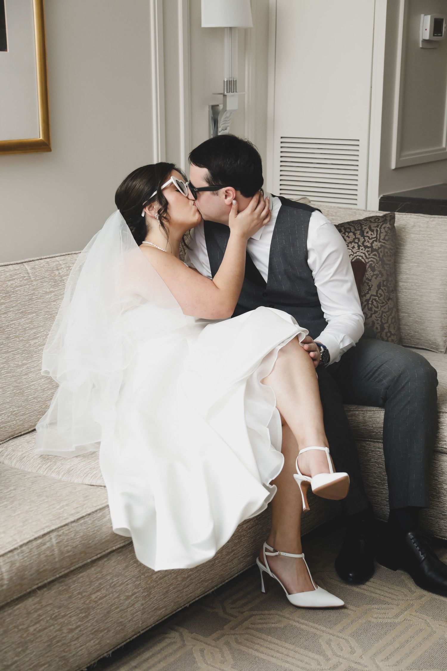 A bride in white wedding dress and groom in black suit sit together on a couch in a sequence of intimate poses.