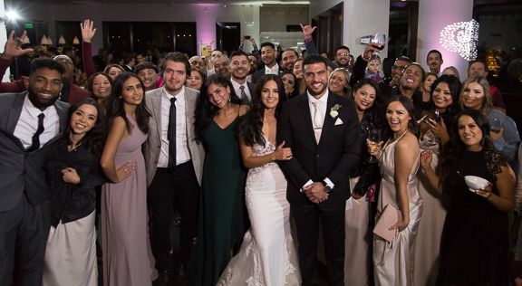Wedding reception crowd celebrates with hands in the air under dramatic lighting.