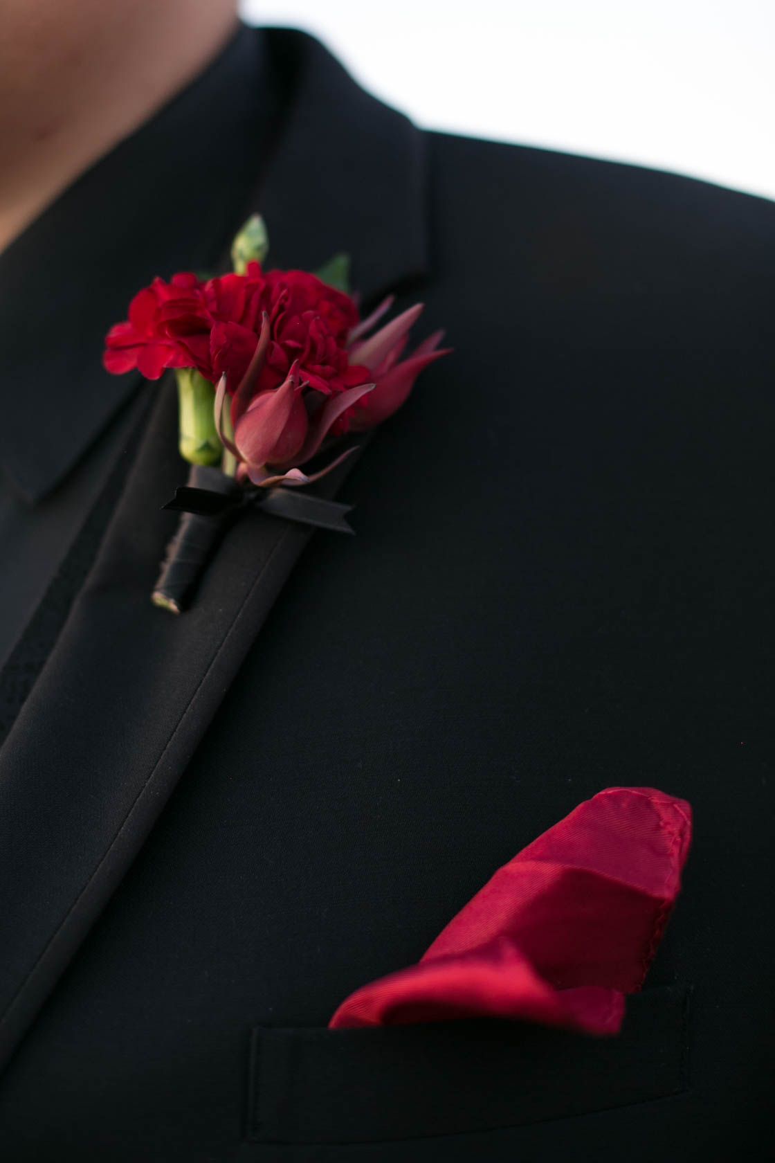 Red rose boutonniere detail shots against black suit jackets show elegant wedding accessories.