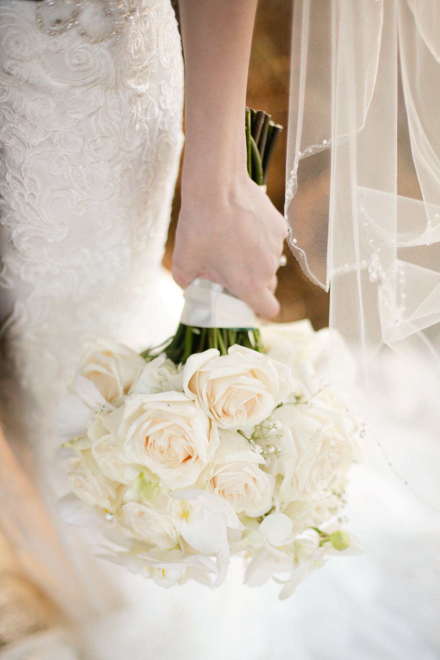 Close-up details of white lace wedding dress with cream roses.