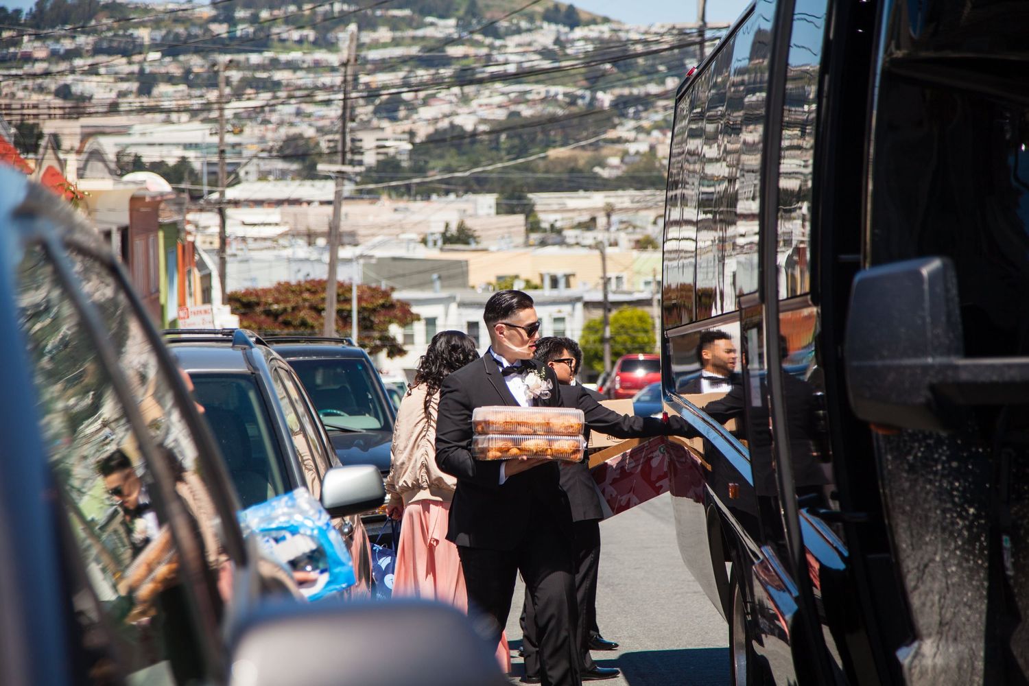 Wedding party members carrying items and supplies through an urban street.