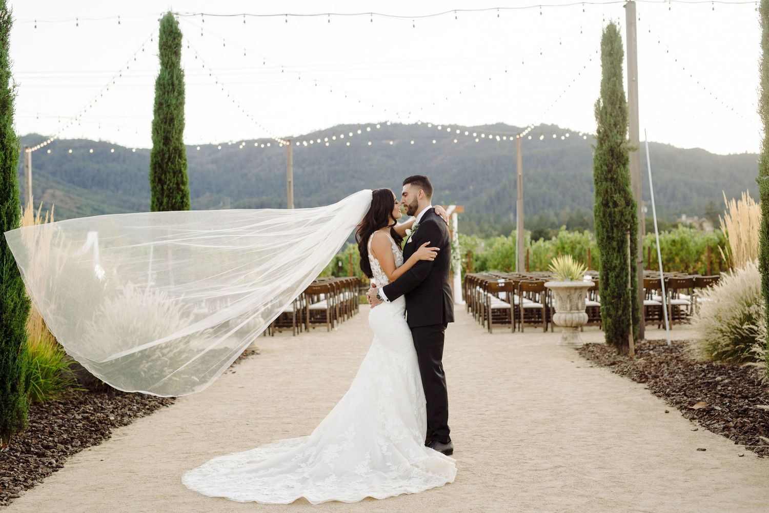 Romantic wedding portraits with flowing veil against mountain landscape and cypress trees.