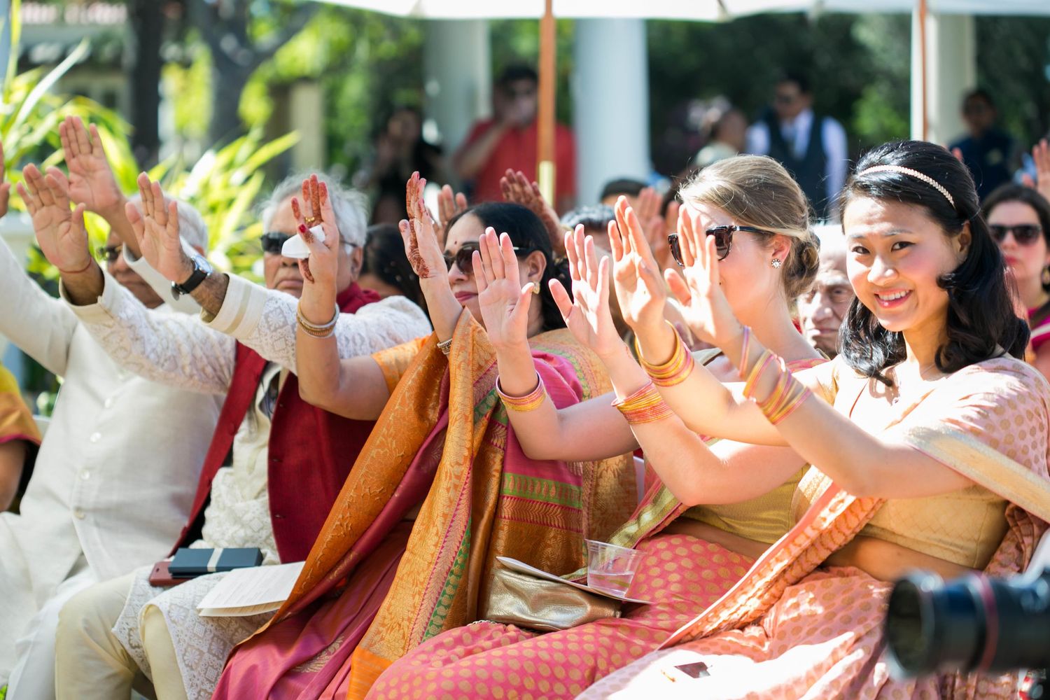Wedding guests celebrating with raised hands during an outdoor ceremony.