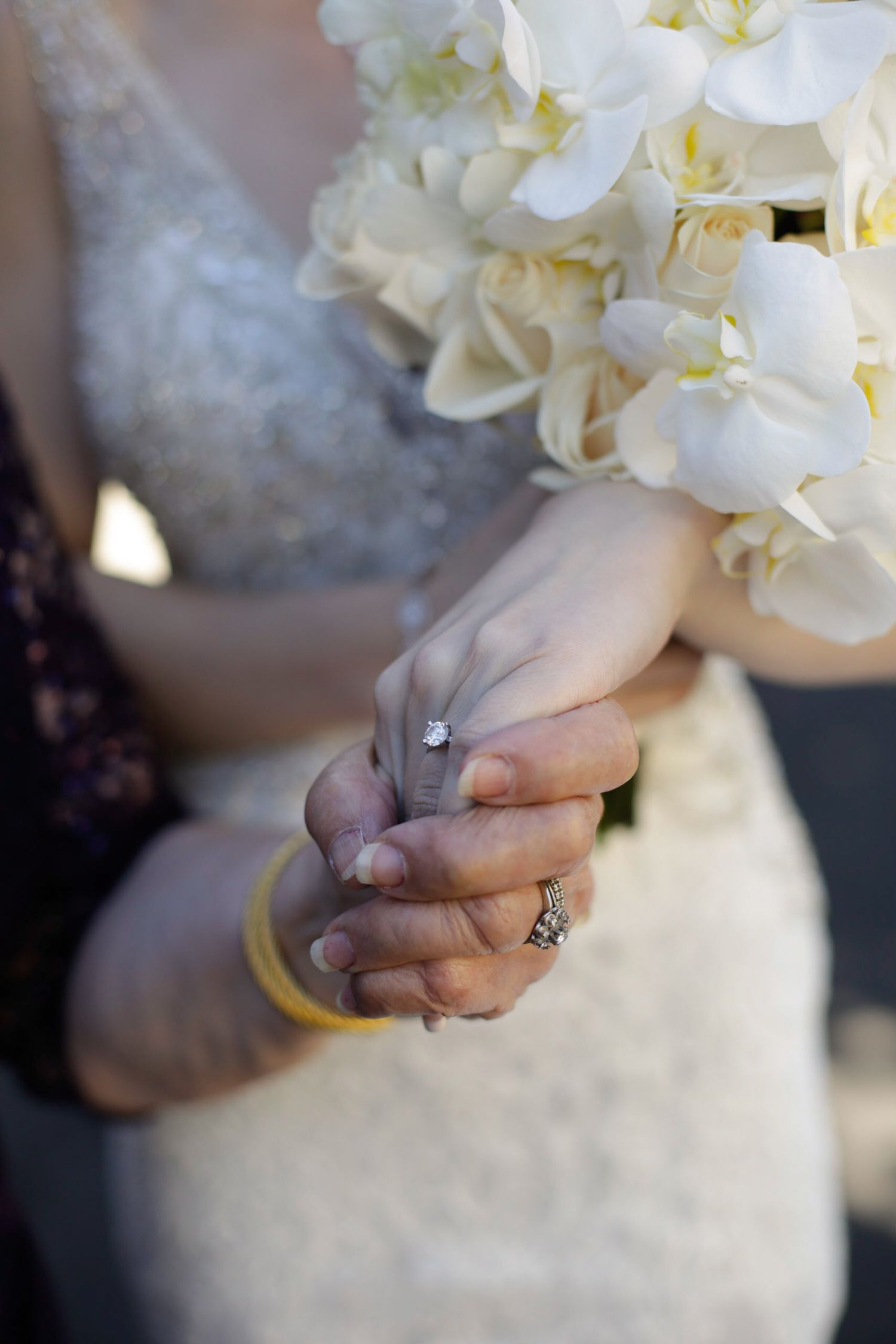 Close-up of white orchid bridal bouquet with hands holding stems.