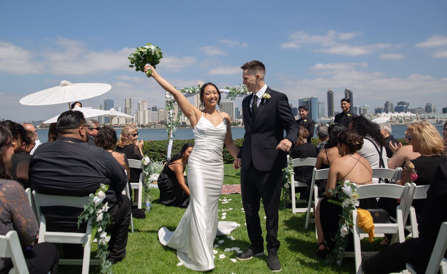 A wedding ceremony on a grassy lawn with white chairs and city skyline views.