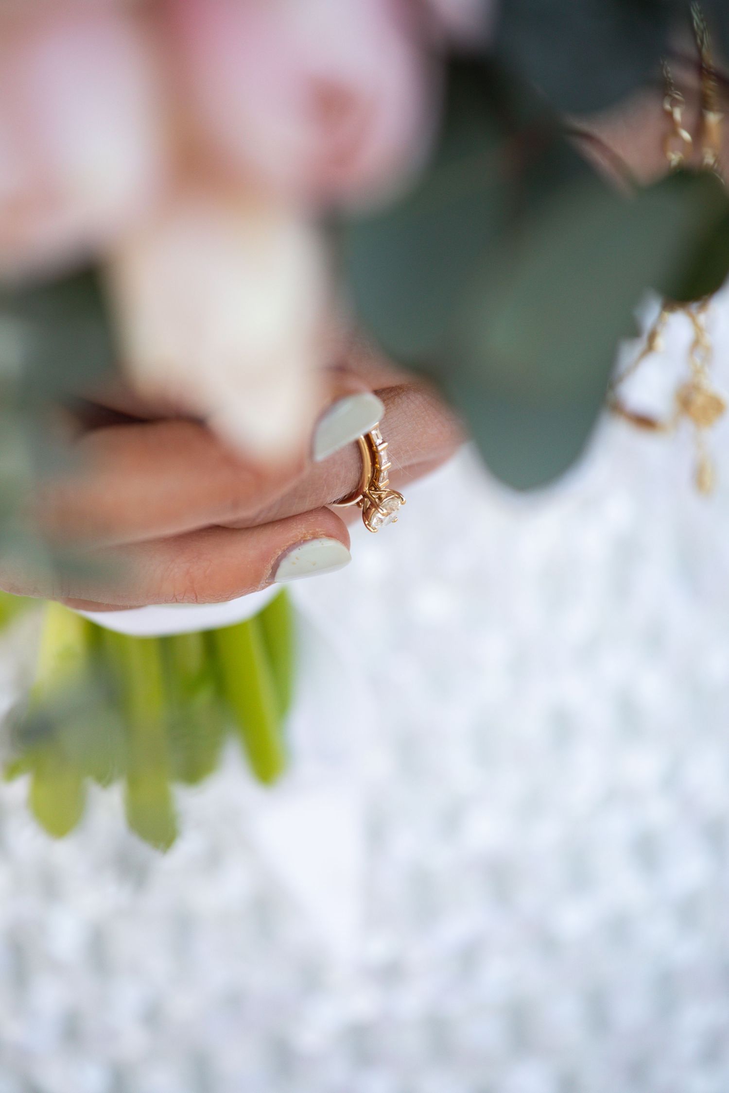 Macro shot of wedding rings with soft bokeh background and green foliage.