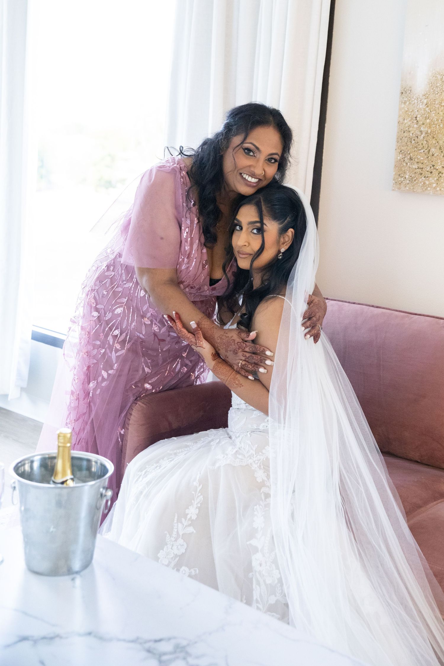Two people share a joyful moment on a pink couch during wedding preparations.