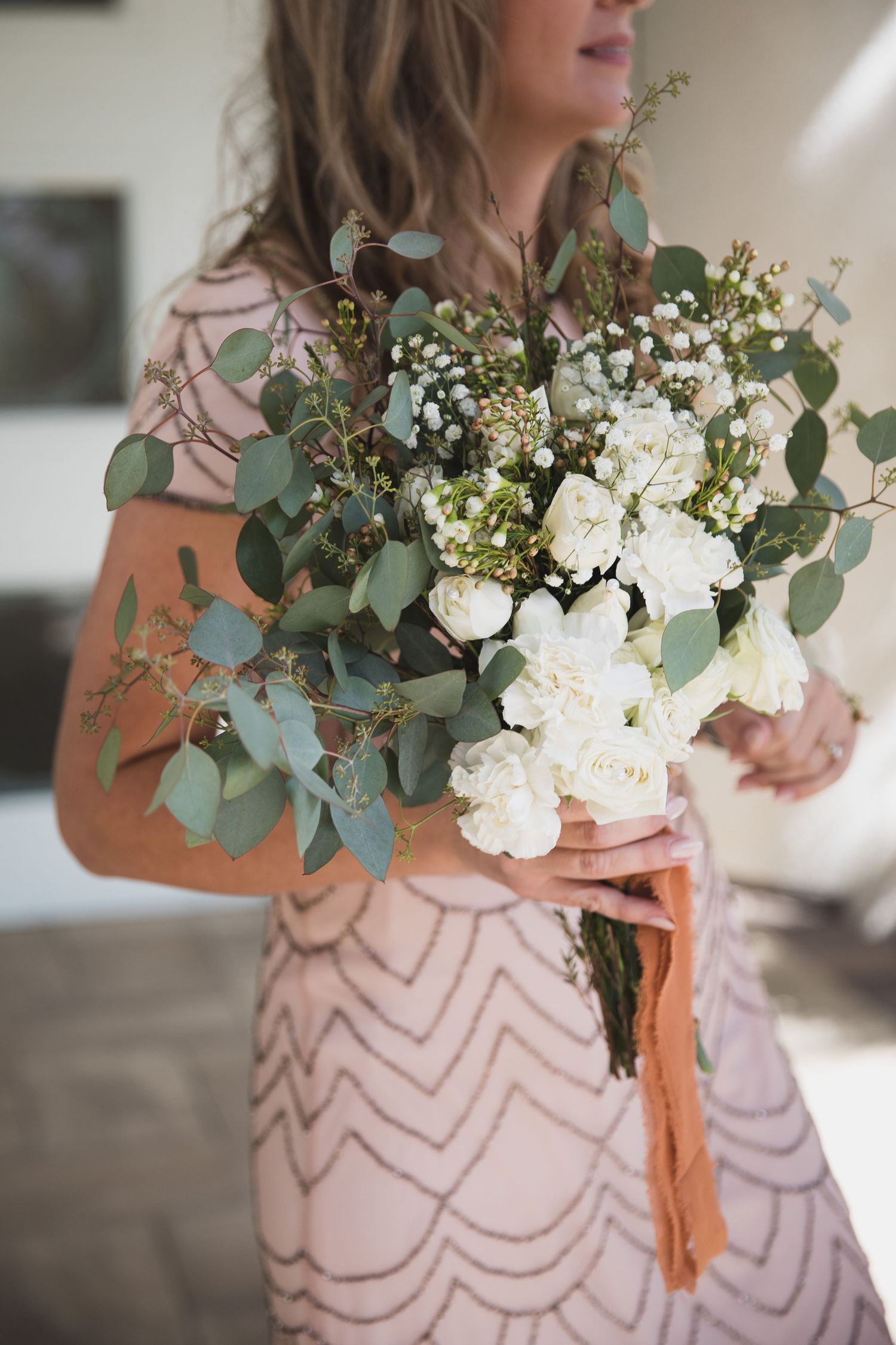 Elegant white and green wedding bouquet with eucalyptus held against geometric patterned dress.