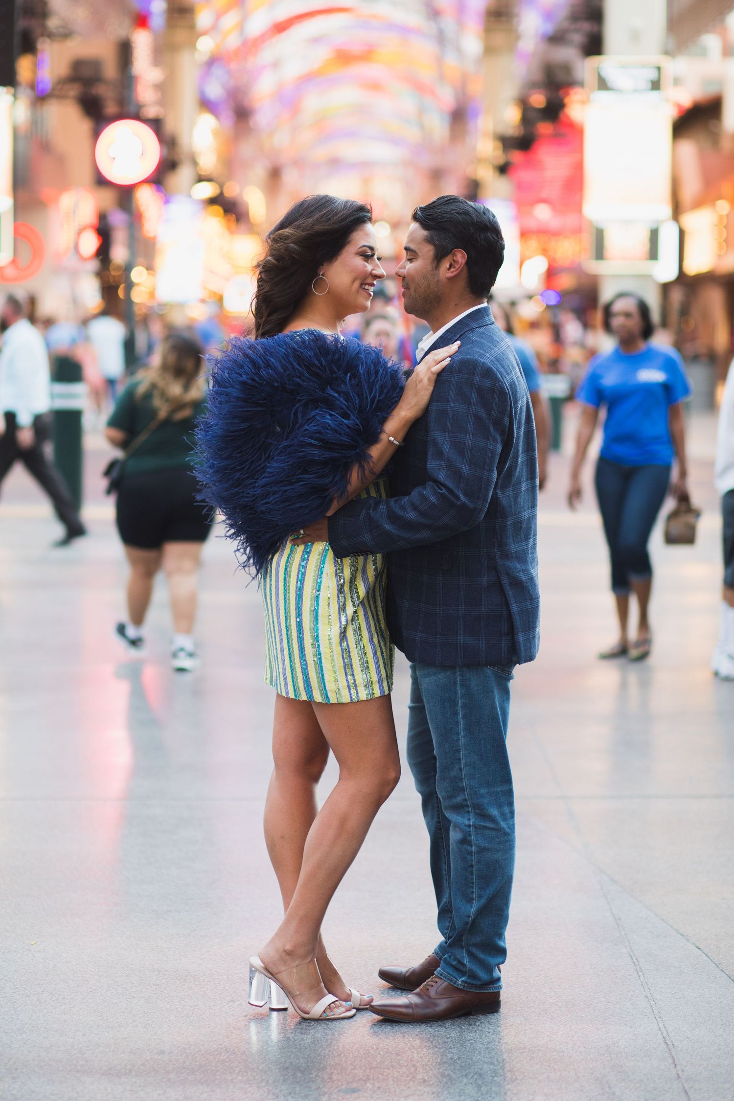 A couple shares an intimate moment on a busy Las Vegas street with colorful lights in the background.