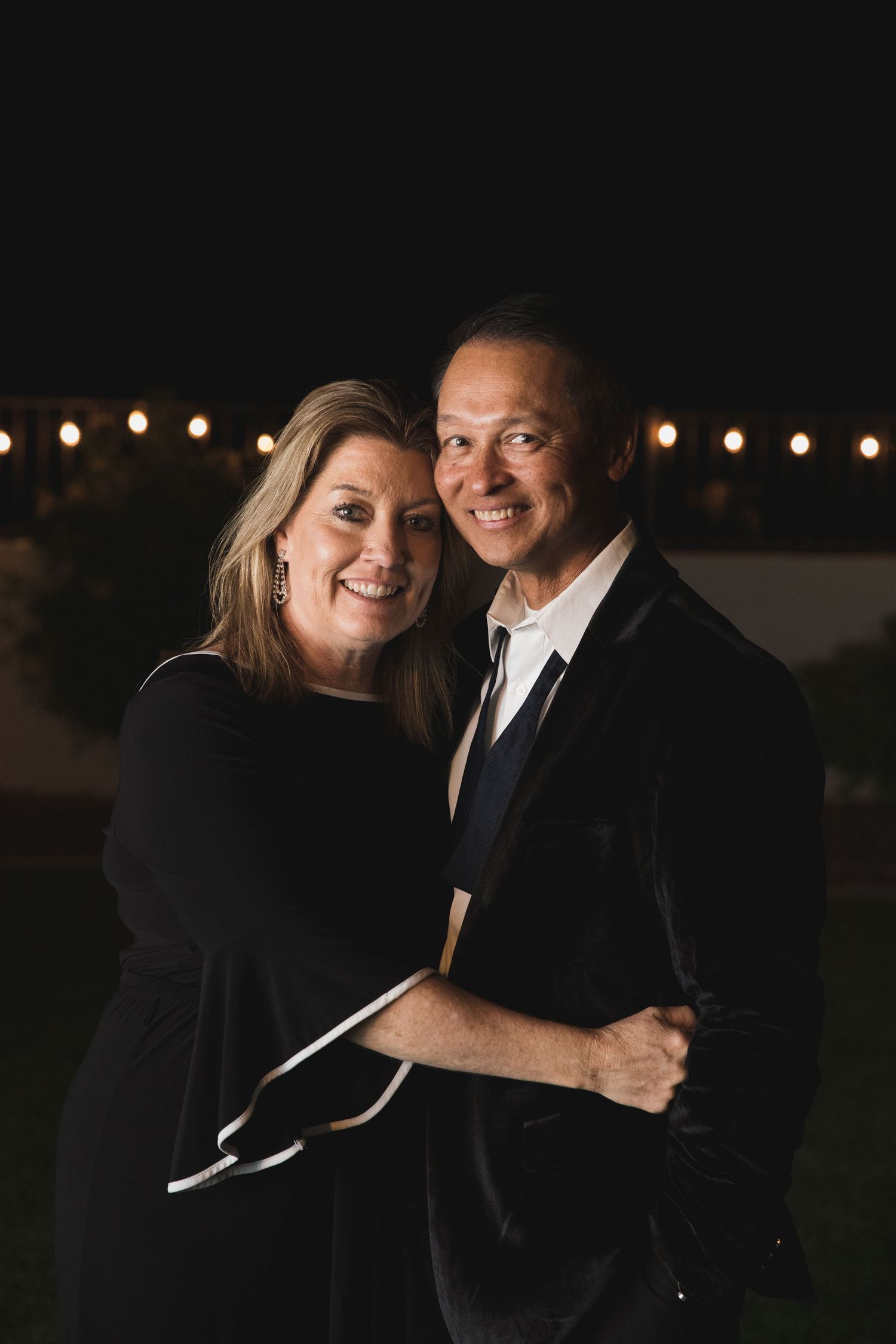 Formal couple shares intimate moment at night under outdoor string lights.