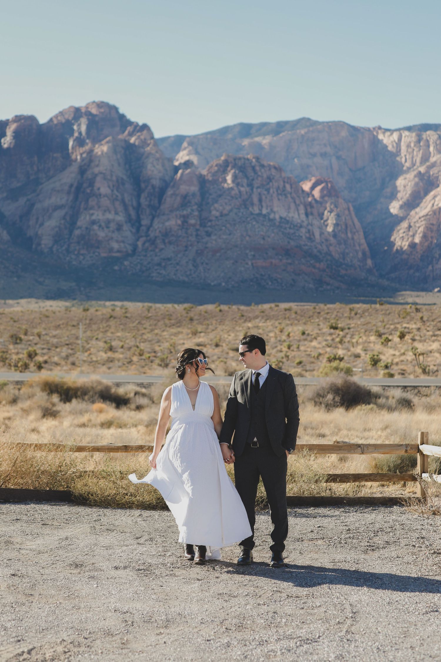 Wedding couple walking together in desert landscape with rocky mountains in the background.
