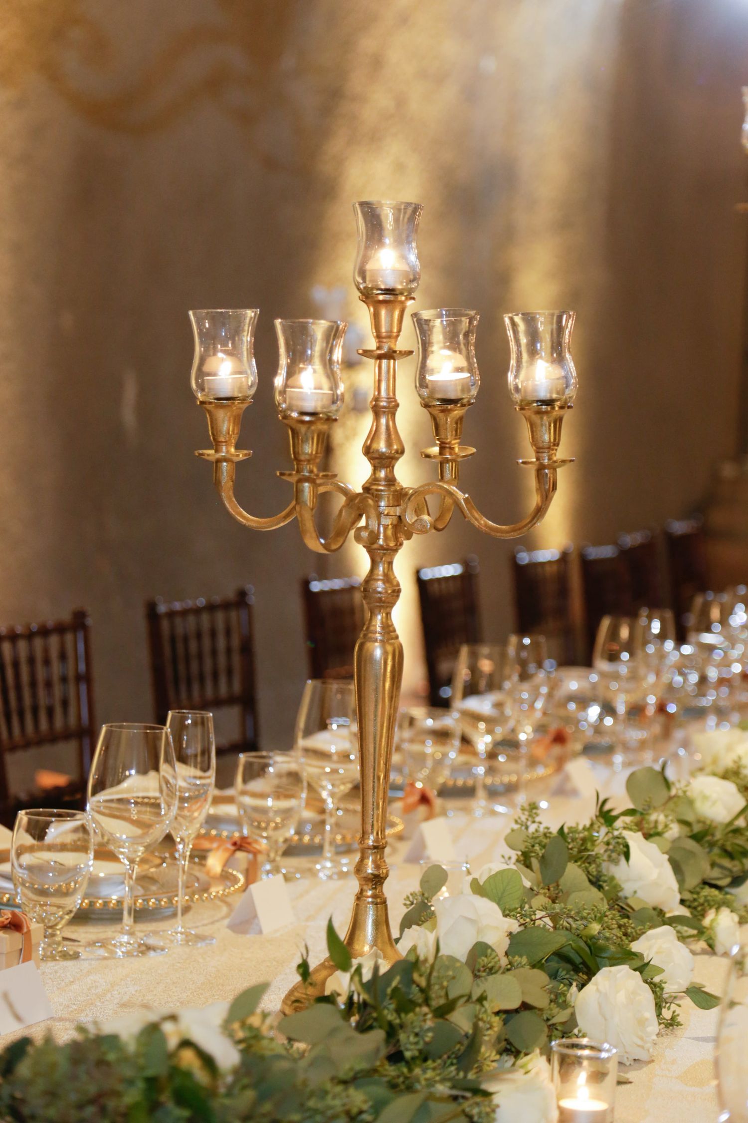 Golden candelabra centerpiece with glowing candles and white floral arrangements on an elegant dining table.