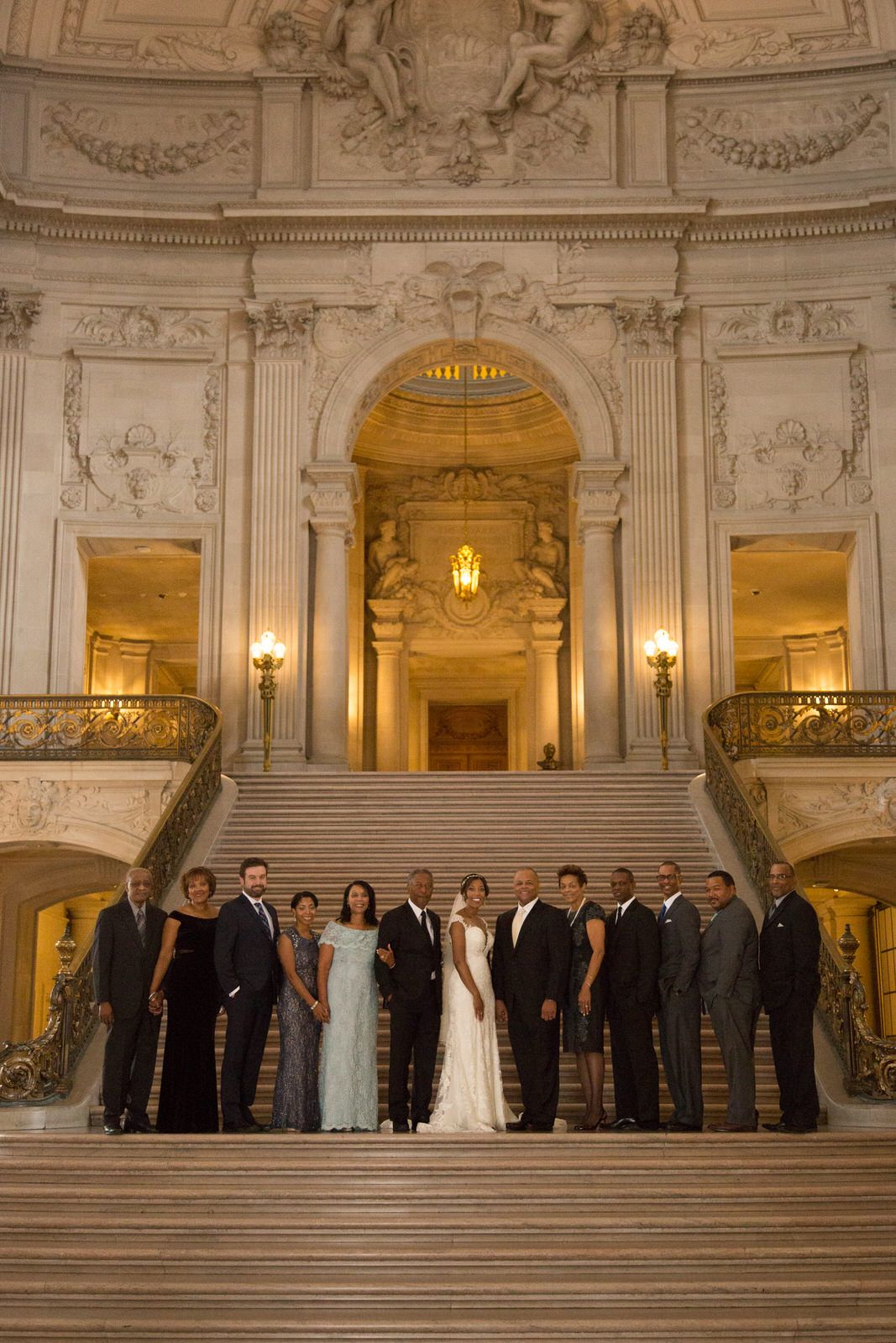 Wedding party lined up on grand marble staircase in elegant historic building.