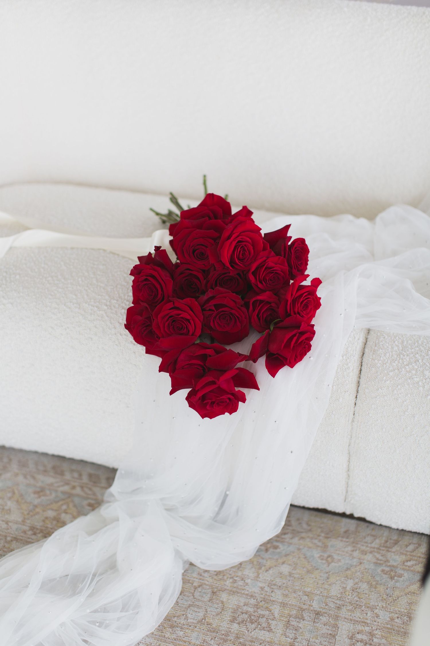 Red roses bouquet draped with white flowing fabric on light background.
